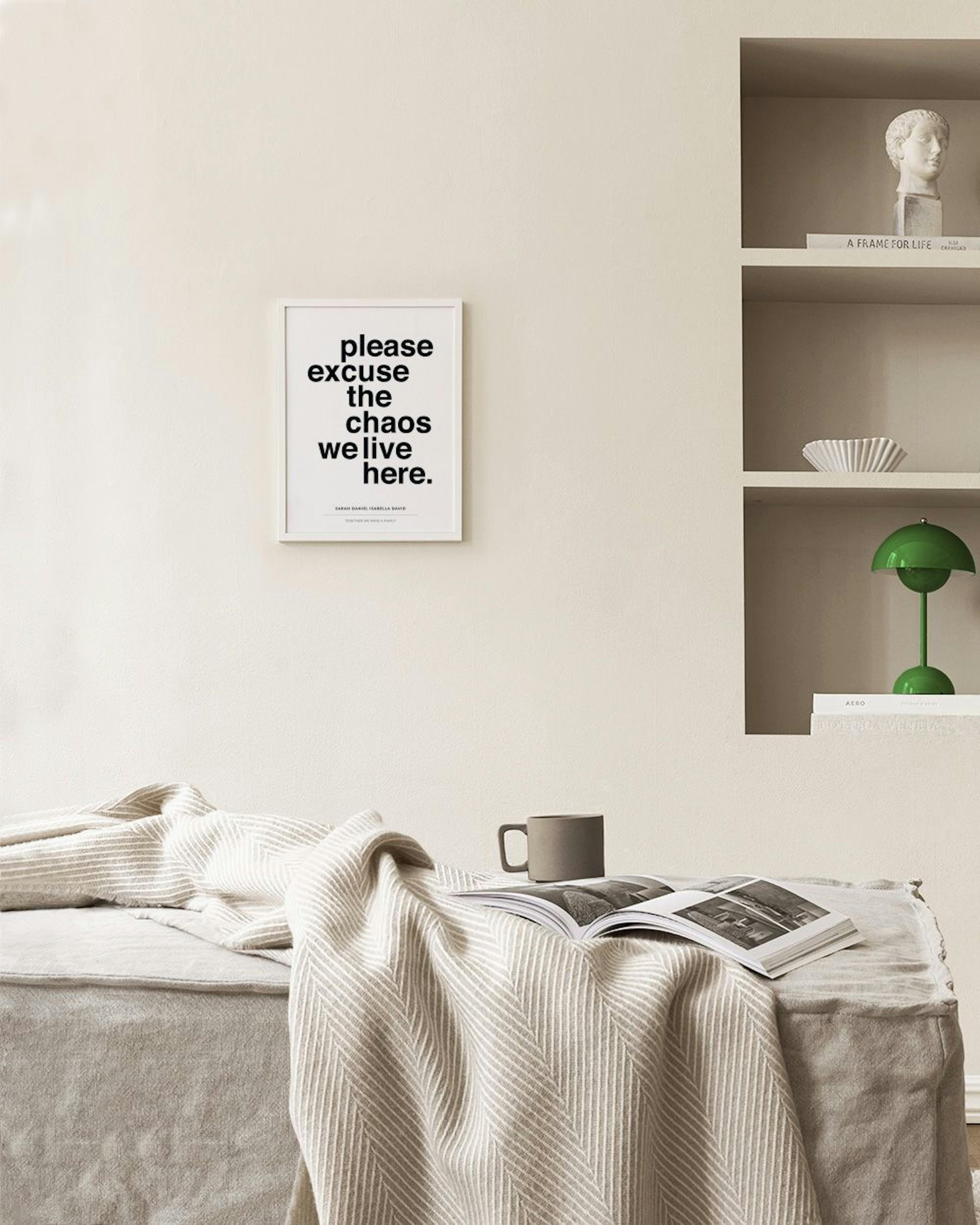 Personalized print with please excuse the chaos we live here text, hanging above a woven rattan cabinet.
