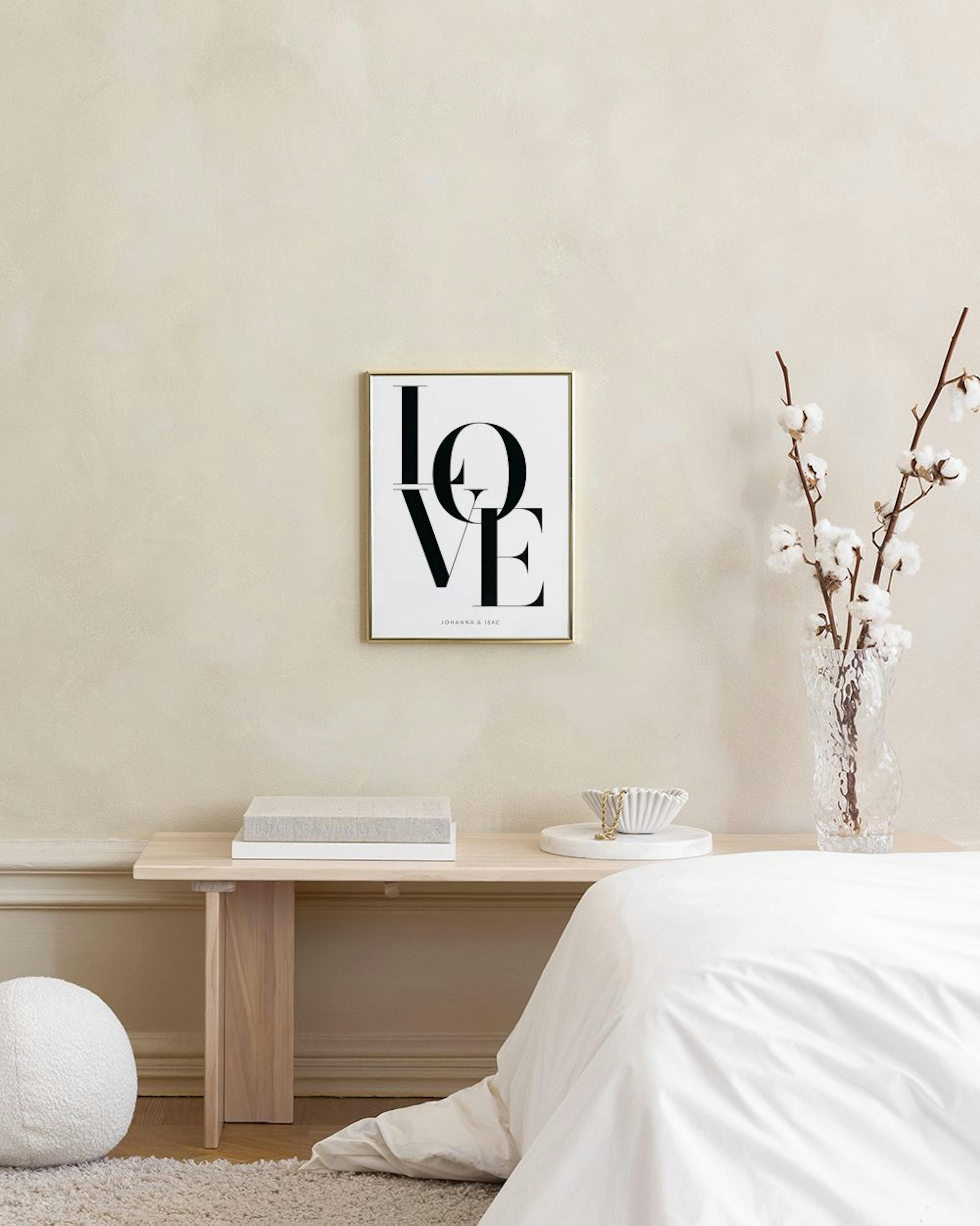 Personlig plakat med sort LOVE tekst og navne, hængende over en rosa velourstol i et lyst rum.