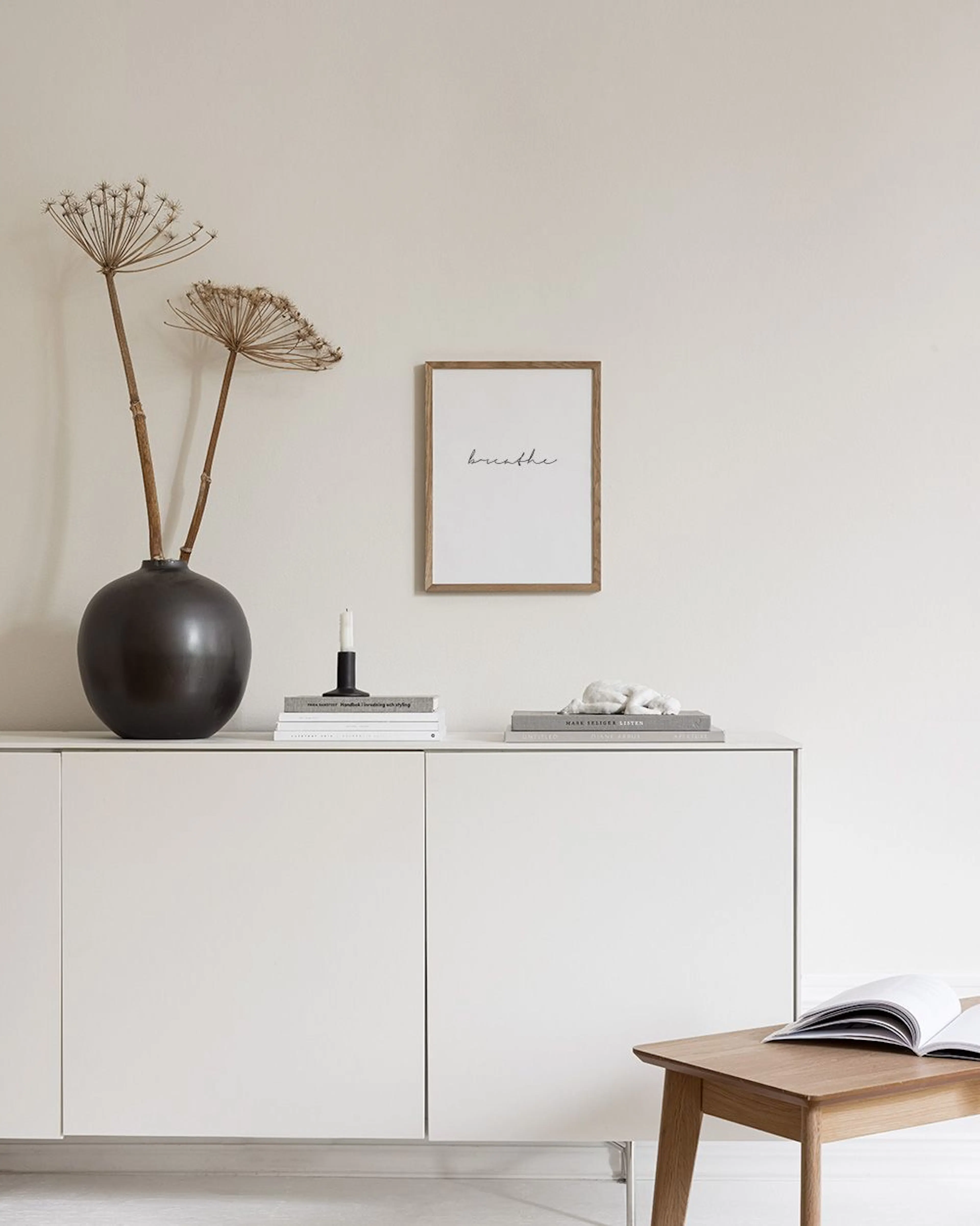 Affiche blanche avec le mot breathe en script noir, suspendue au-dessus dun banc en bois avec des vases, des coussins et une cou