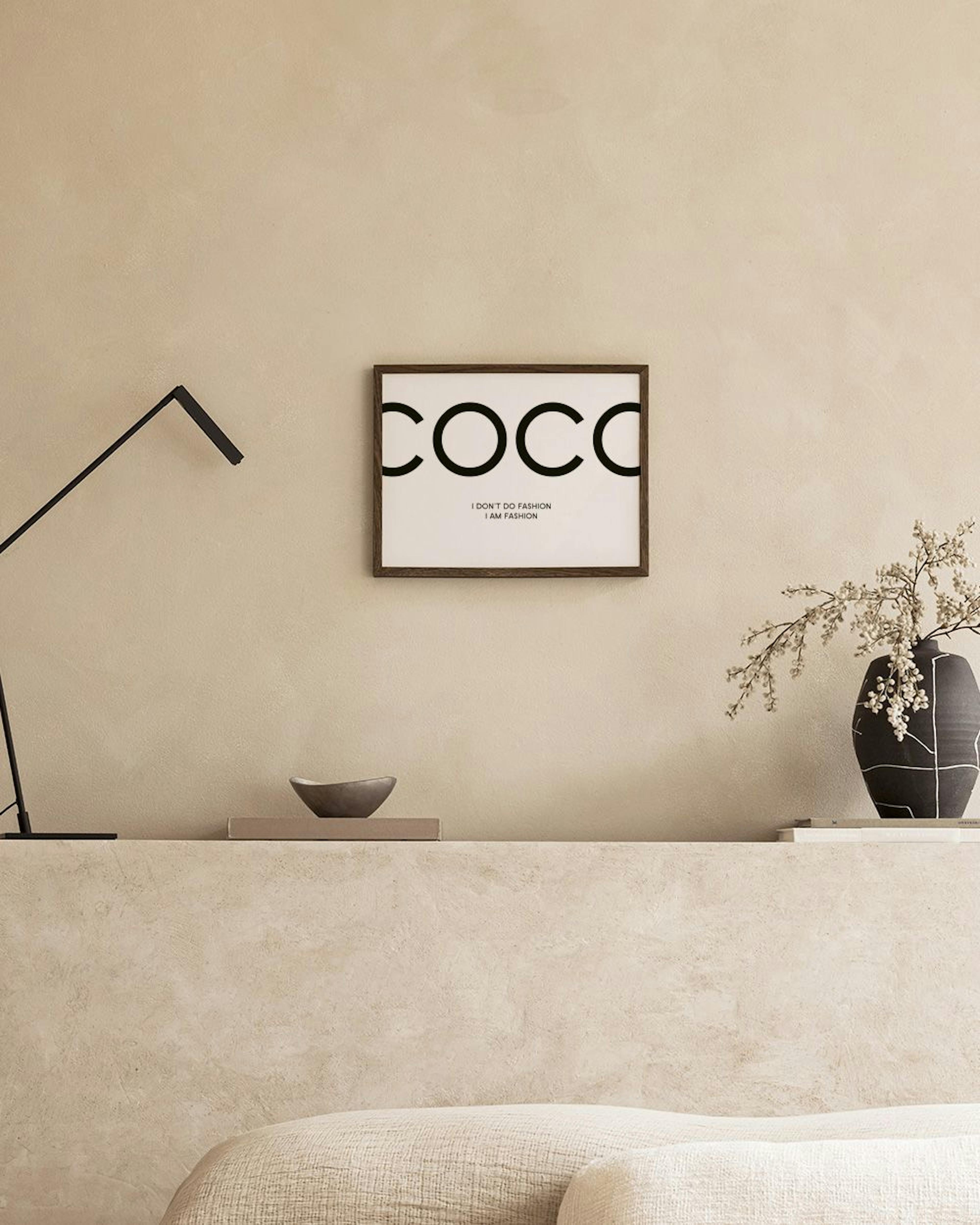 A minimalist print with COCO in large black letters and I DONT DO FASHION I AM FASHION below, displayed above a black side table