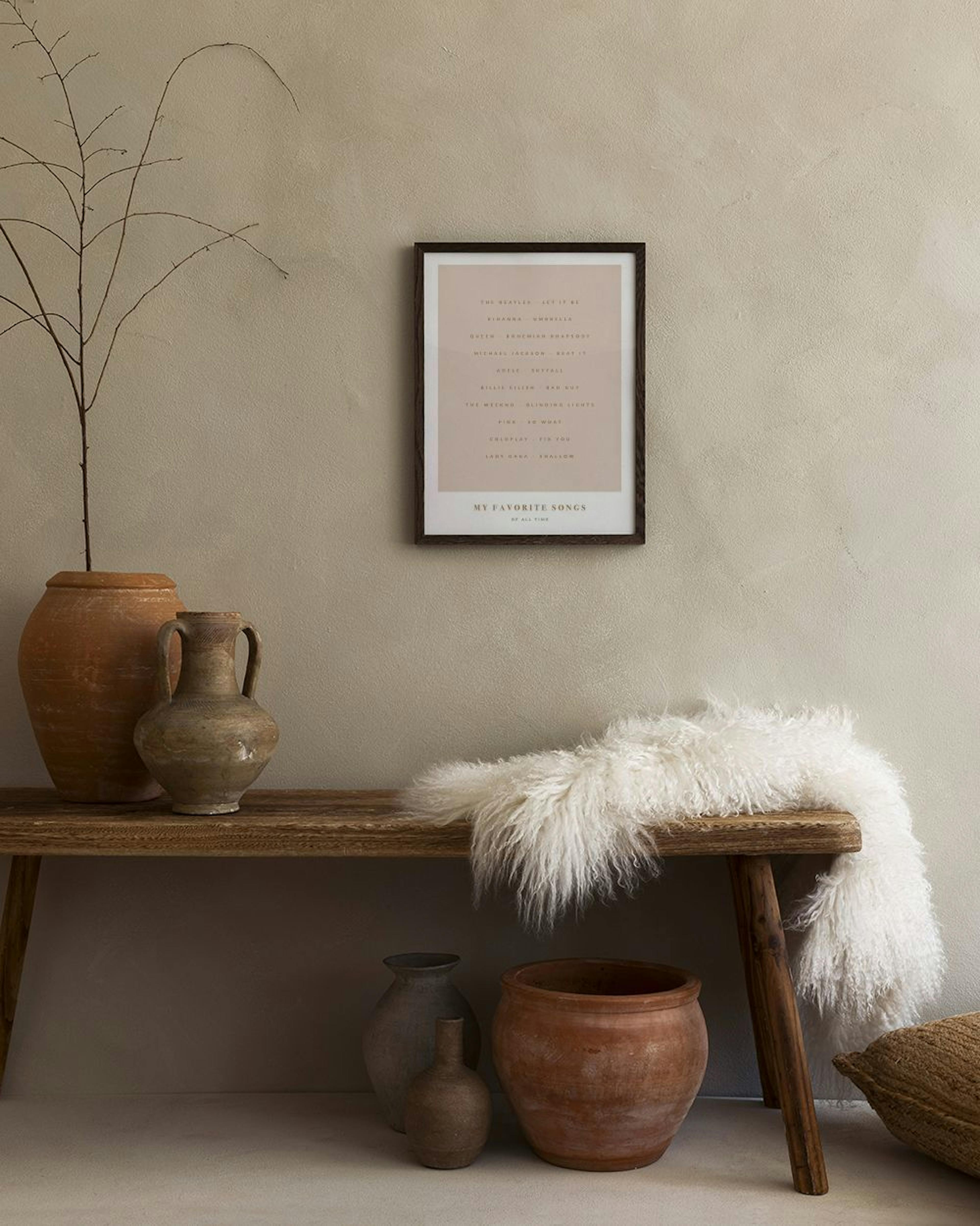En personlig plakat med My Favorite Songs og kunstnernavne på en lyserød baggrund, hængende over et lyst træbord med en lampe.