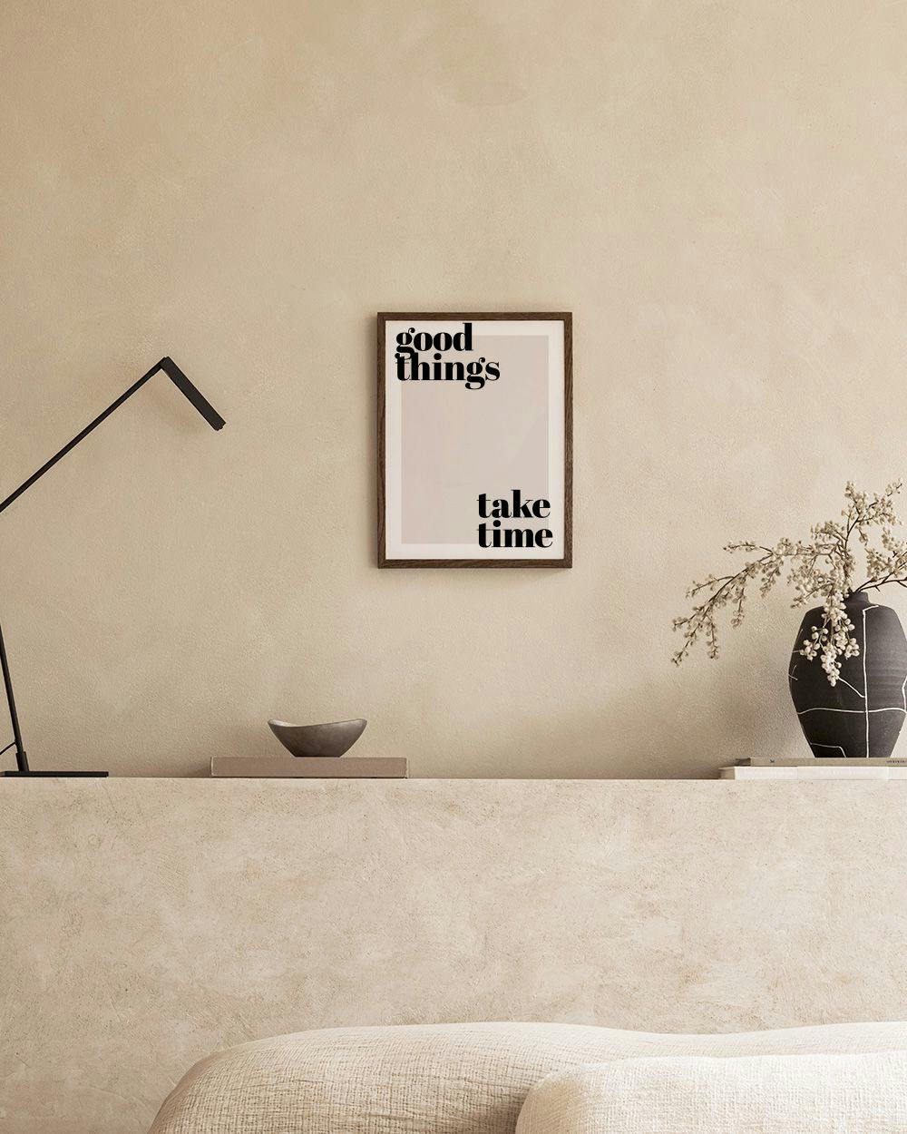 「good things take time」と書かれた白黒のポスターが、棚の上の白いランプとオブジェと共に飾られた部屋の様子。