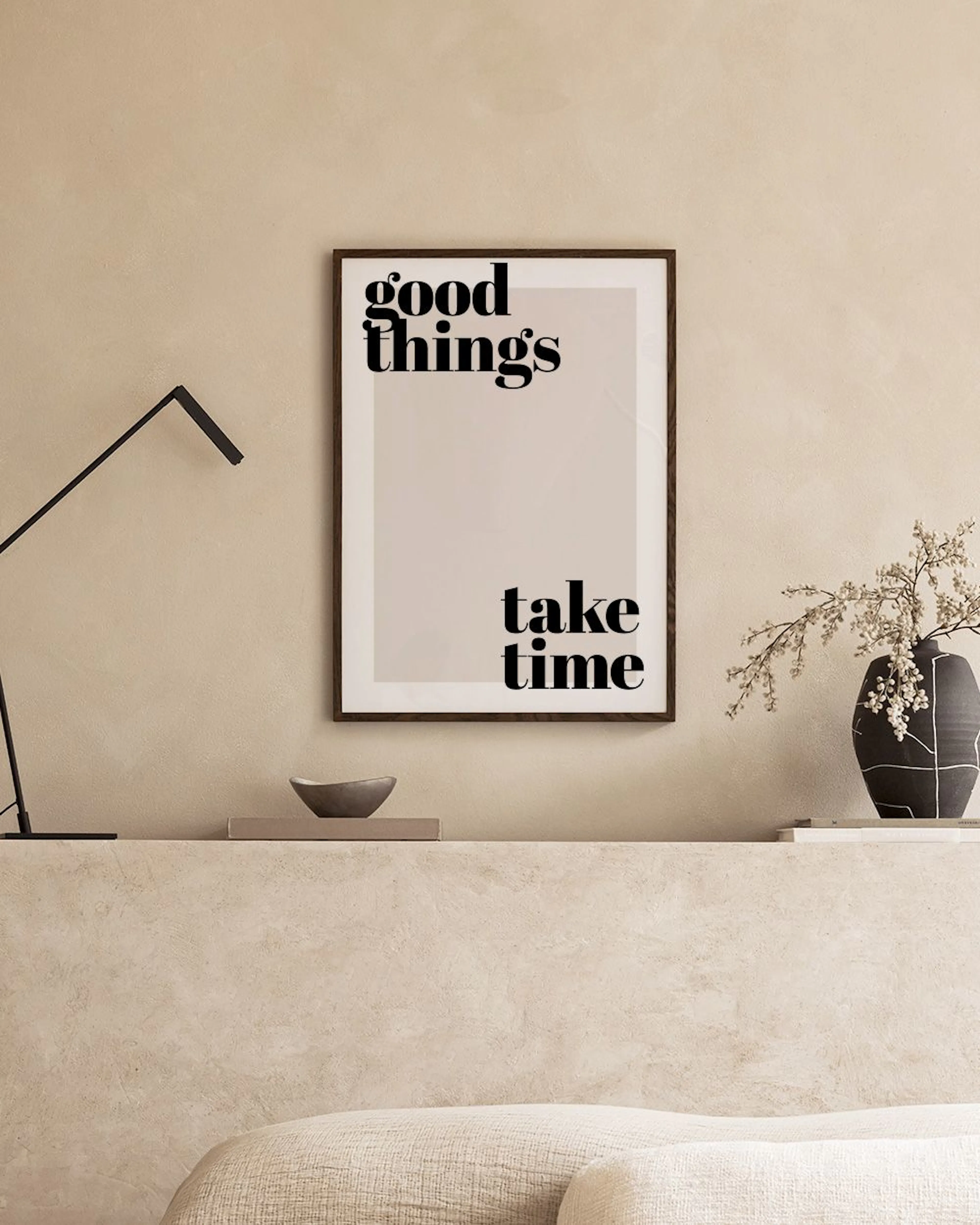 Poster con scritta good things take time su parete chiara, sopra una mensola nera con lampada e decorazioni.