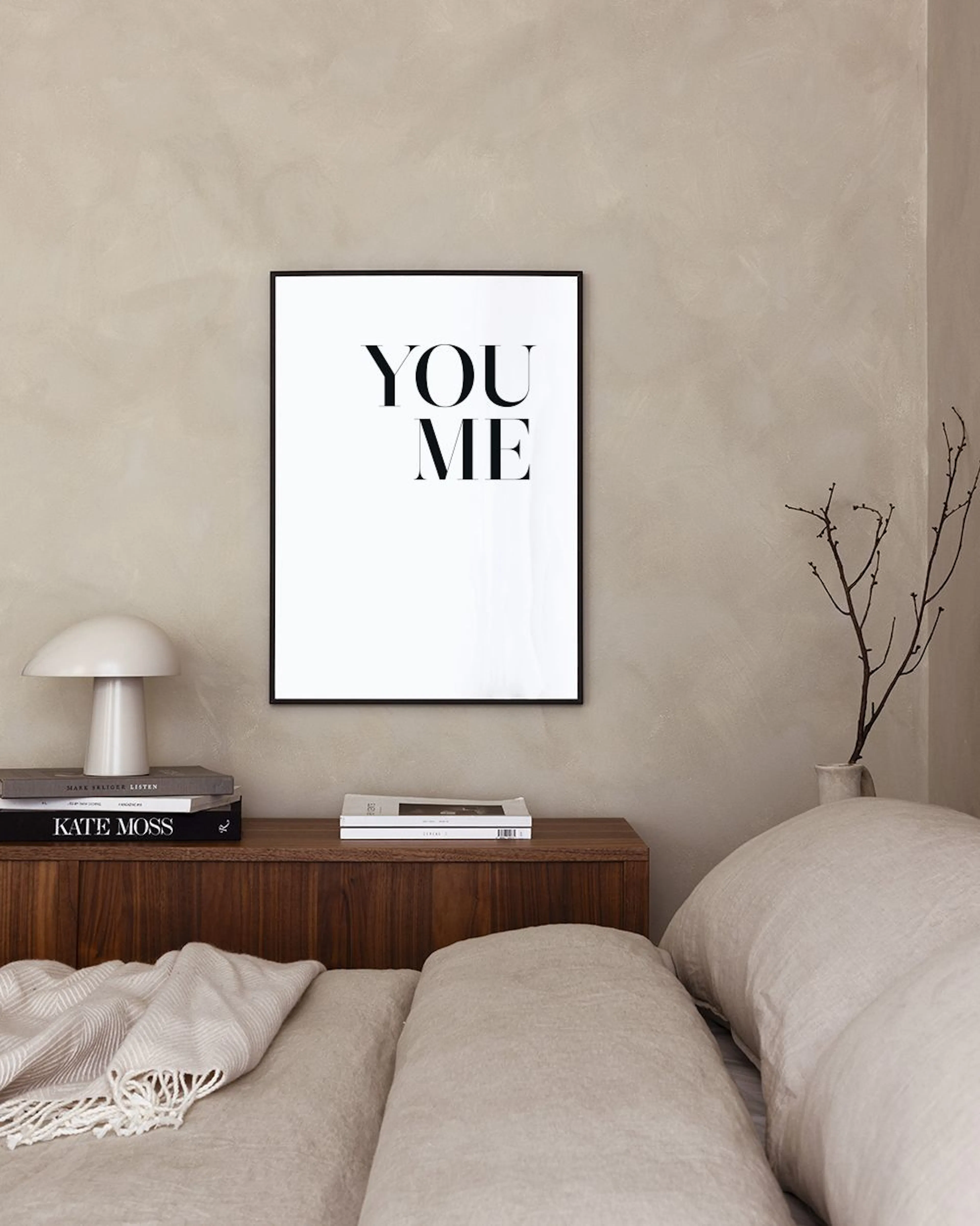 Mustavalkoinen typografinen juliste tekstillä YOU ME, ripustettuna makuuhuoneen sängyn yläpuolelle.