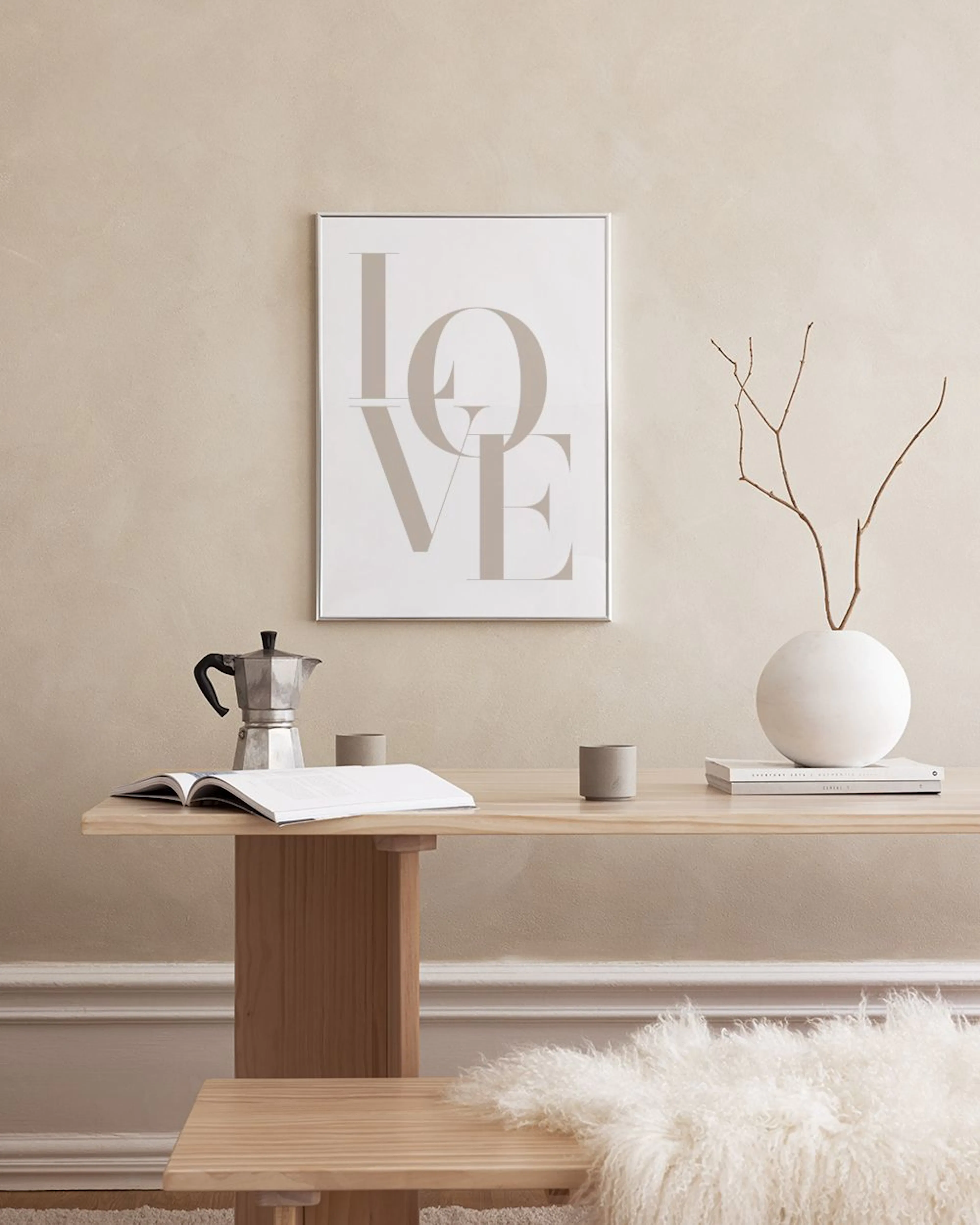 A print with the word LOVE in large beige serif letters hanging above a white console table with books and decorative vases.