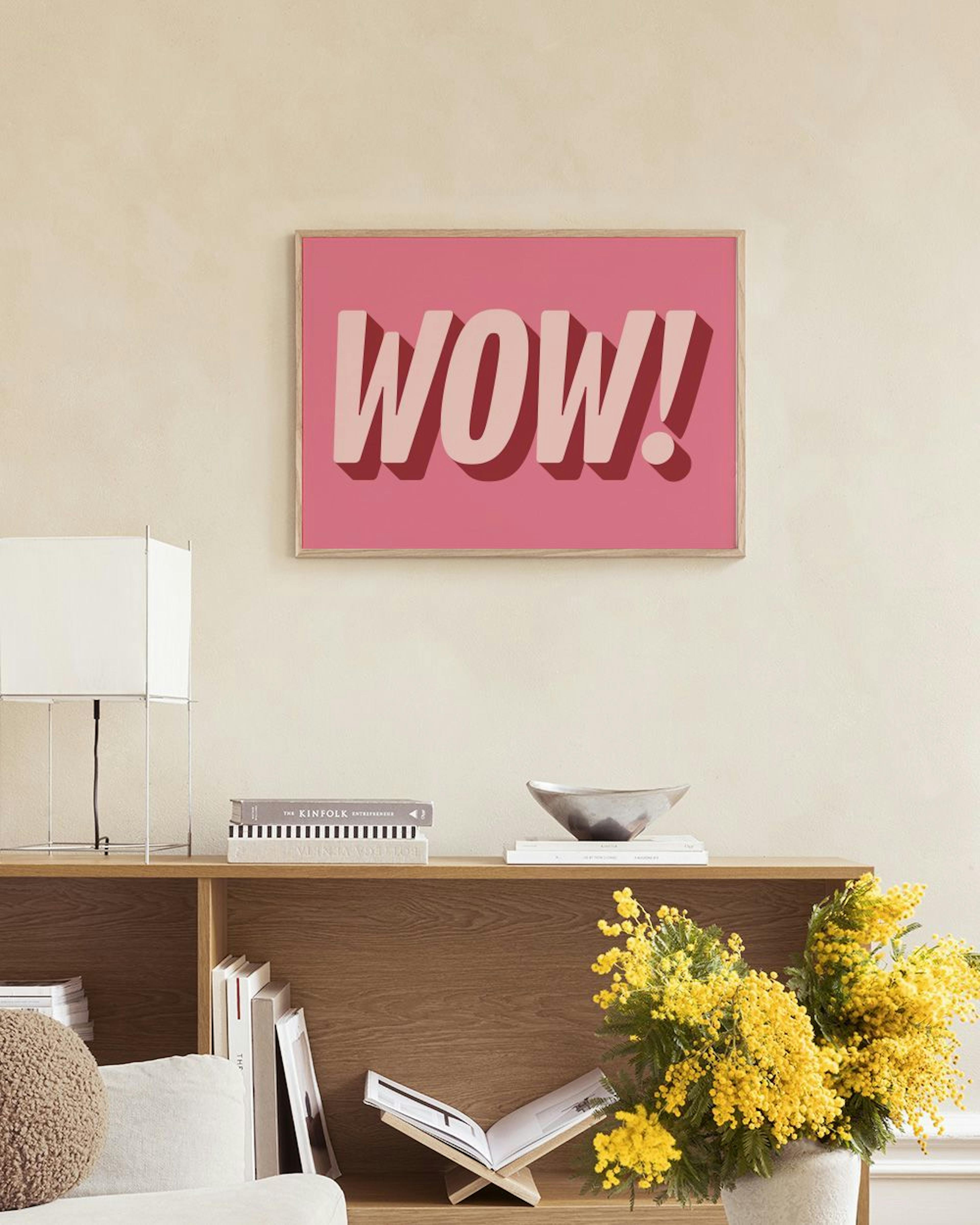 Póster rosa vibrante con la palabra WOW! en letras 3D color rosa claro, exhibido sobre un estante negro con libros y accesorios 