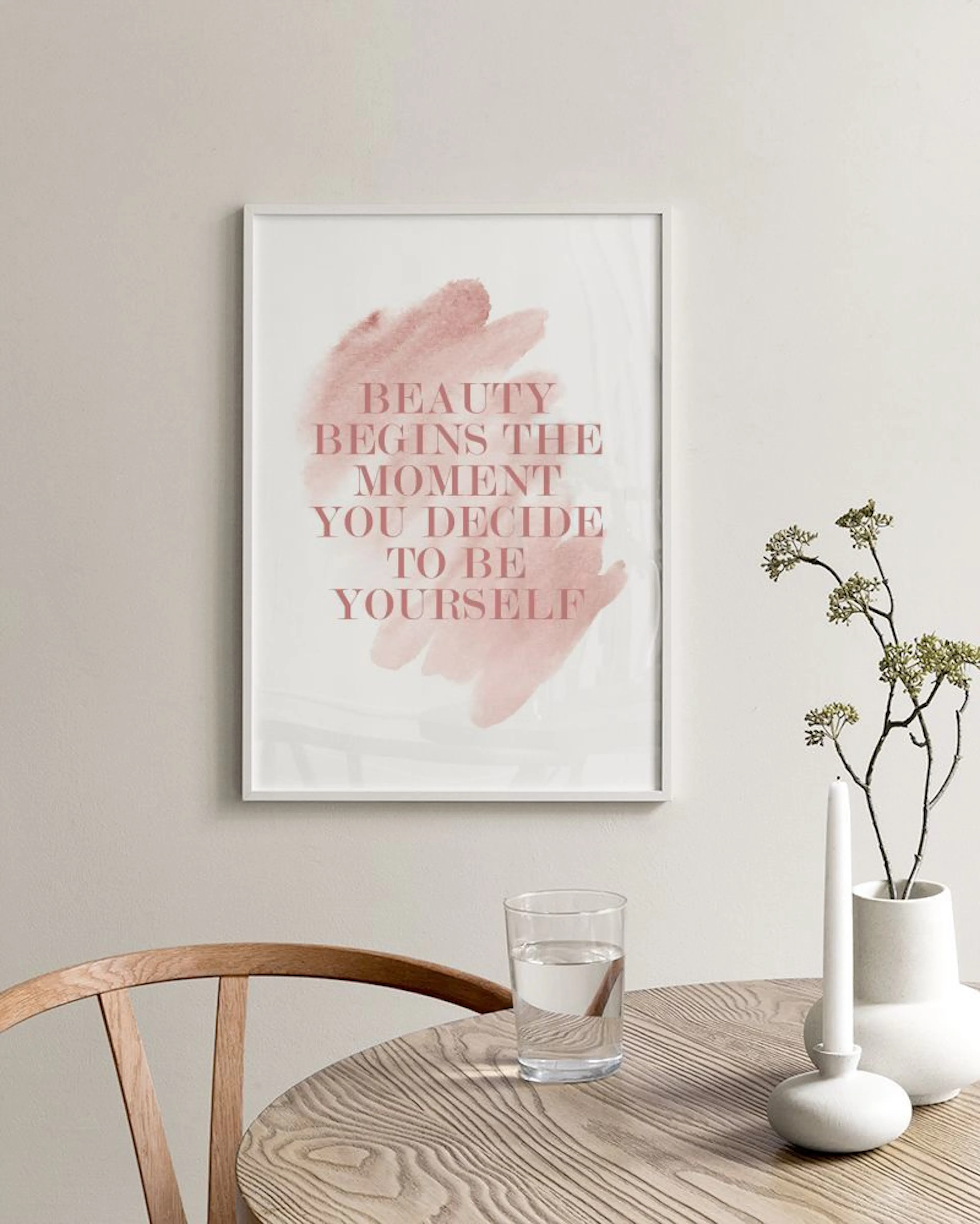 Plakat z różowym napisem BEAUTY BEGINS THE MOMENT YOU DECIDE TO BE YOURSELF na tle akwareli, stojący na czarnej półce z książkam