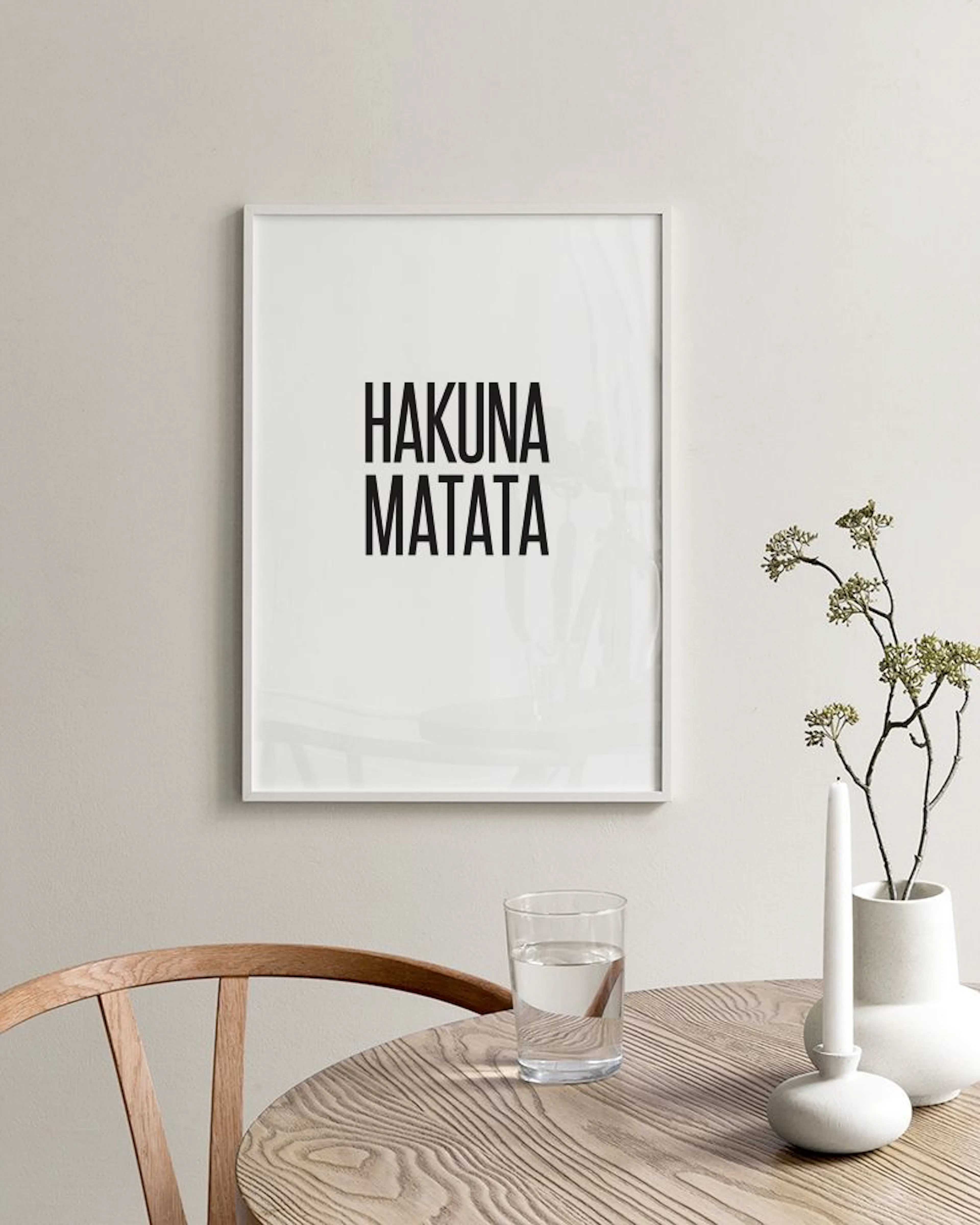 A minimalist print with HAKUNA MATATA text in black, hanging above a white cabinet with paint brushes and a woven basket.
