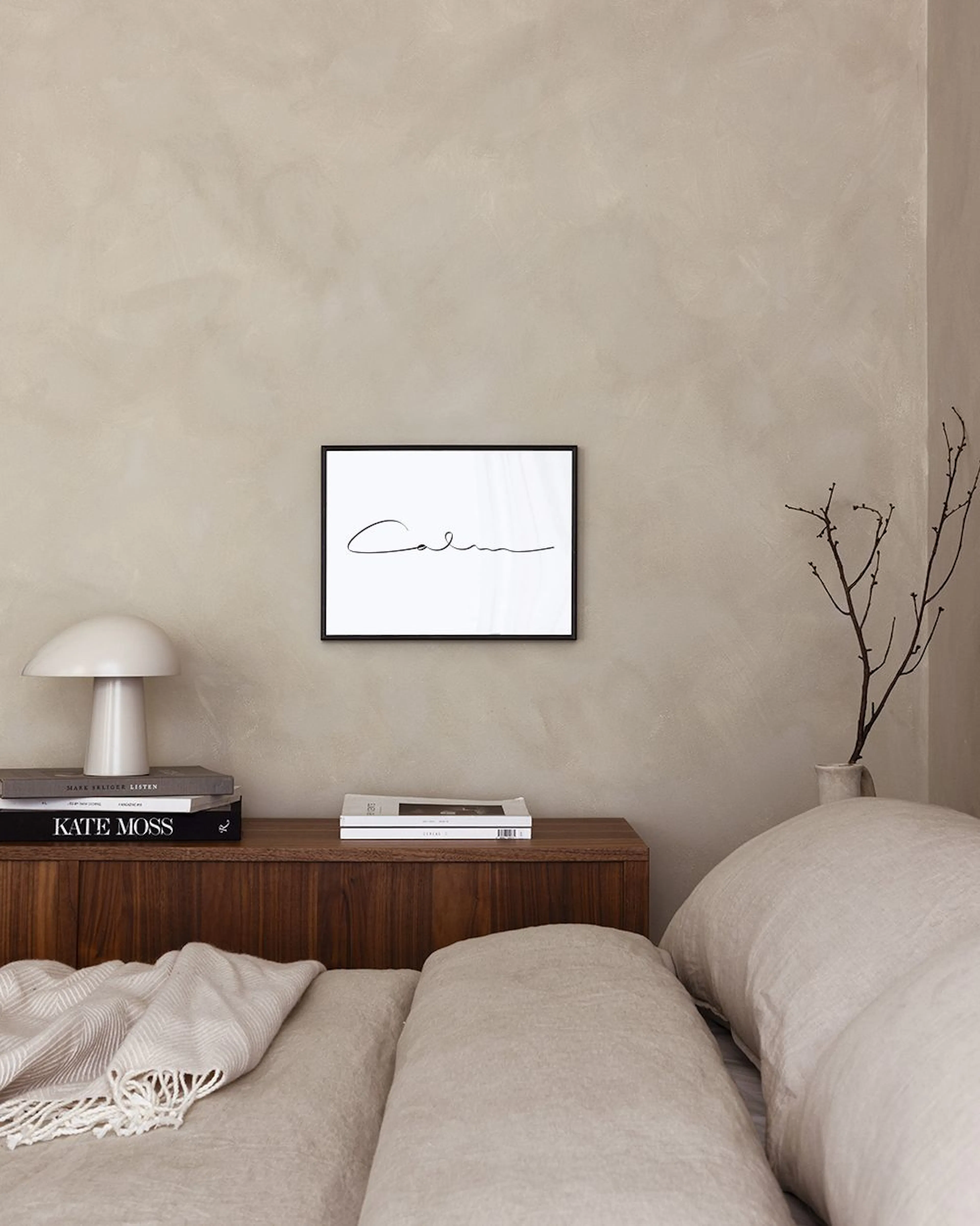 Affiche murale avec le mot Calm calligraphié en noir, affichée dans un salon moderne aux murs roses.