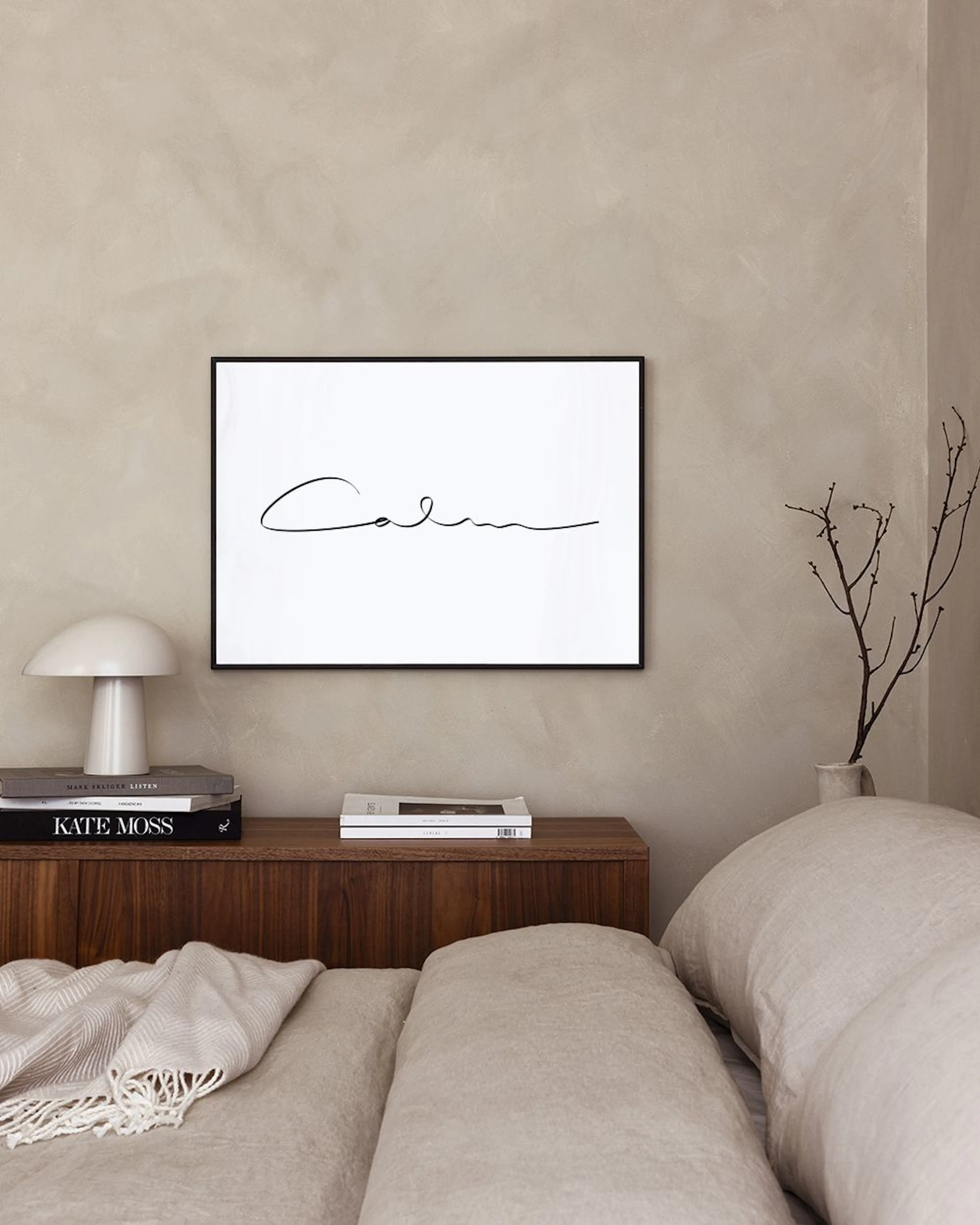 A print with the word Calm in black script on a white background, hanging on a light pink wall above a pink velvet ottoman.