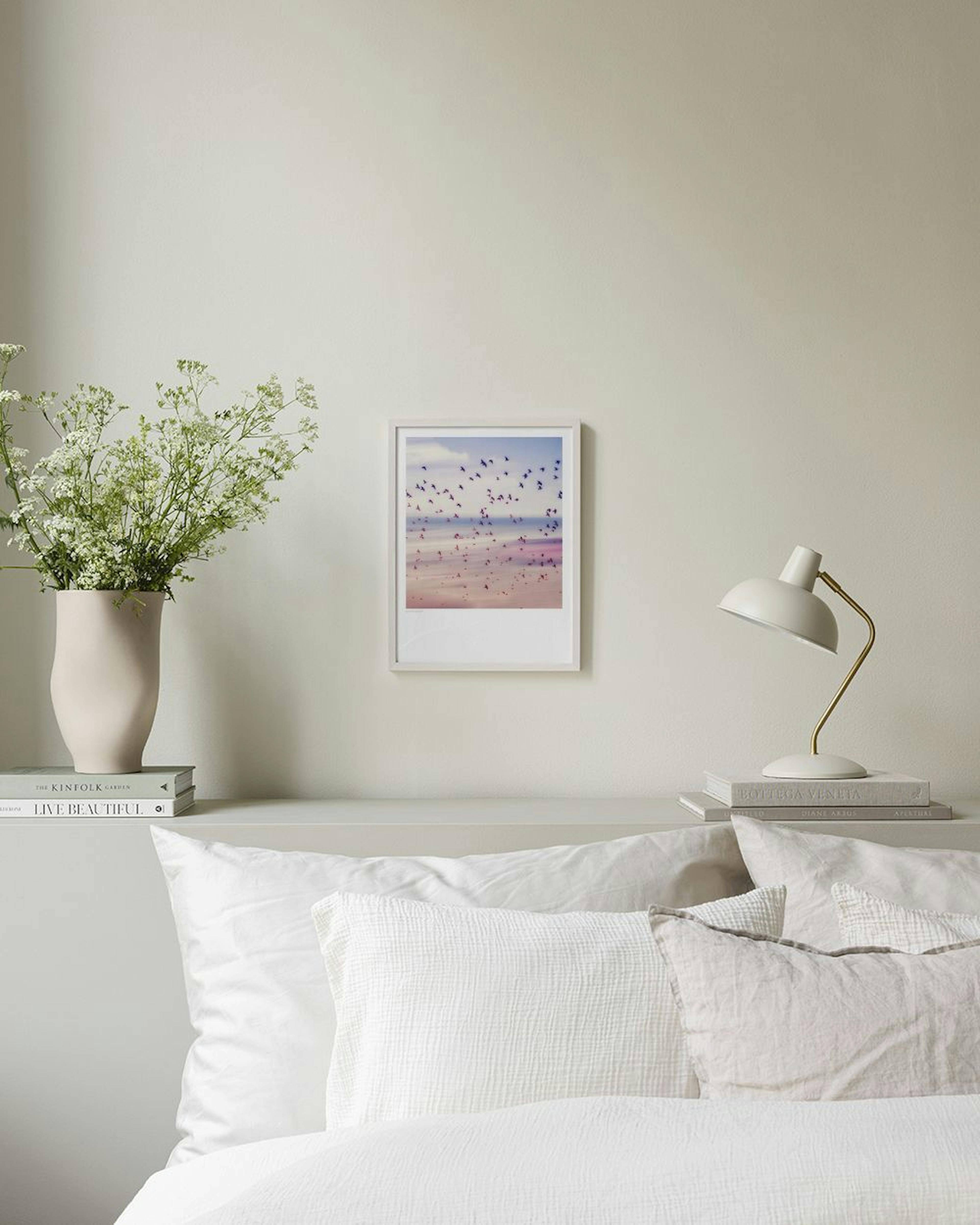 Plakat med foto af en flok fugle over en lyserød og beige strand, hængende over et gråt skab med vaser.