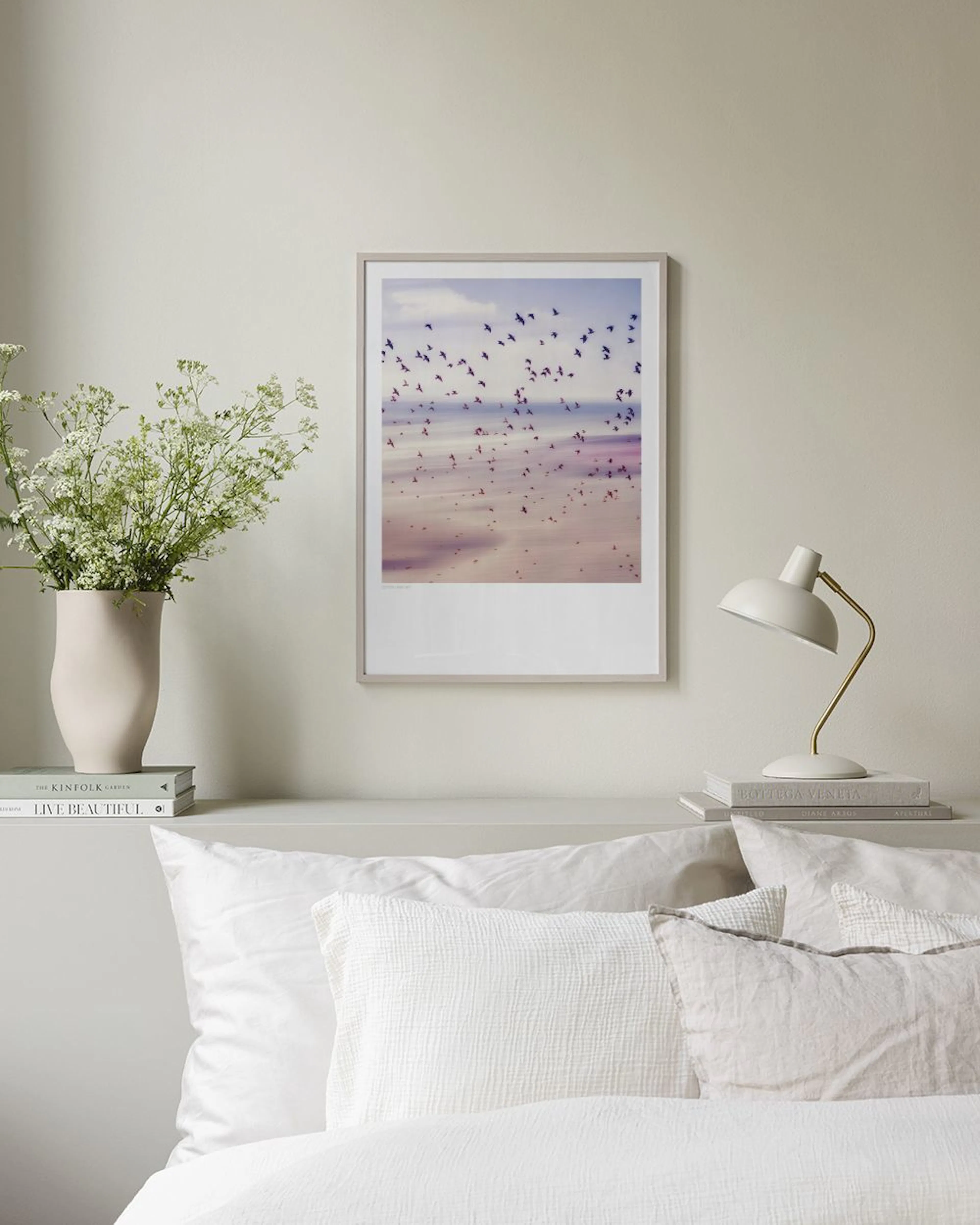 A print of a pink and purple beach scene with flying birds, displayed above a dark grey cabinet with decor.