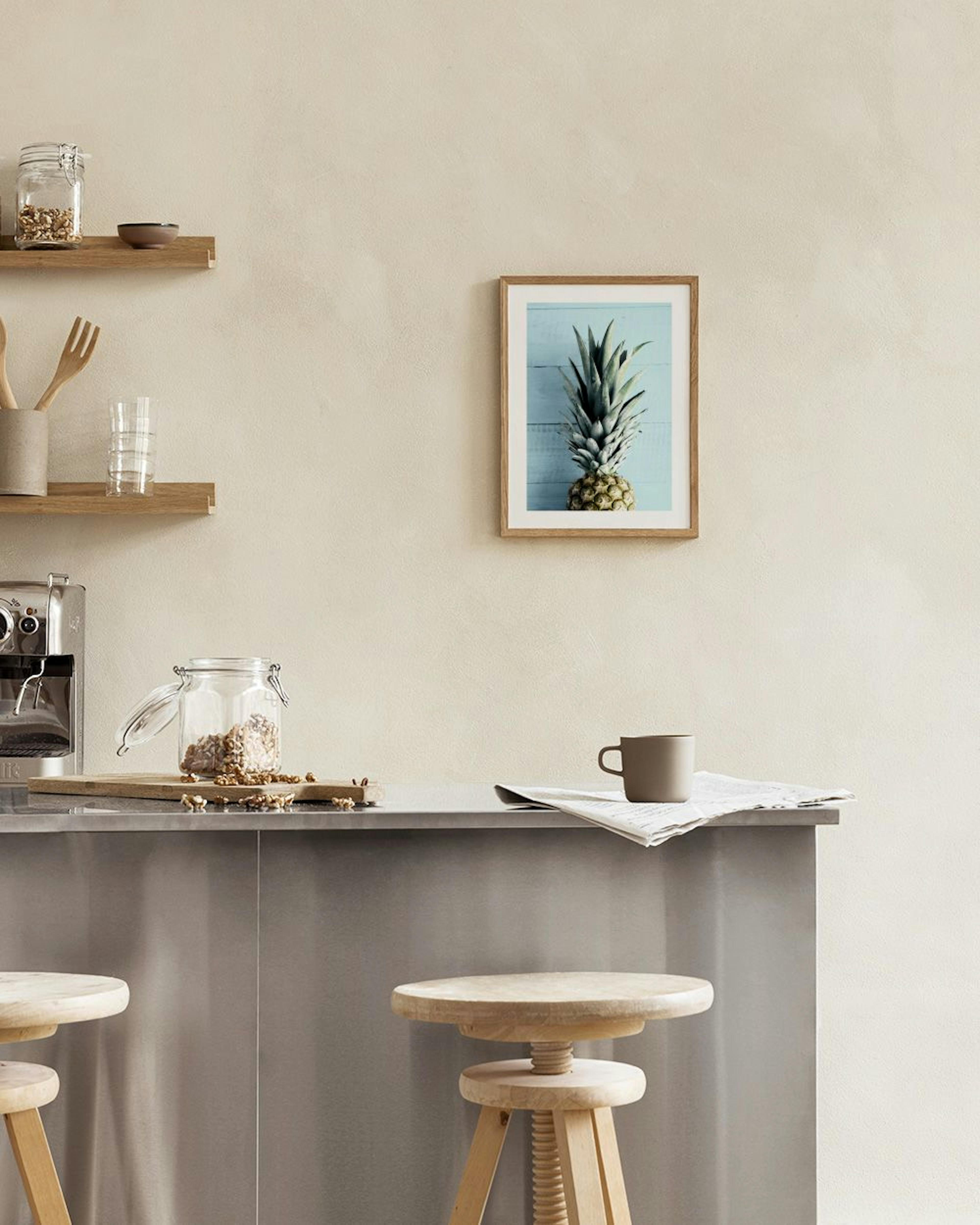 Póster de una piña sobre un fondo azul claro de madera, colgado en una pared blanca sobre una mesa de comedor.