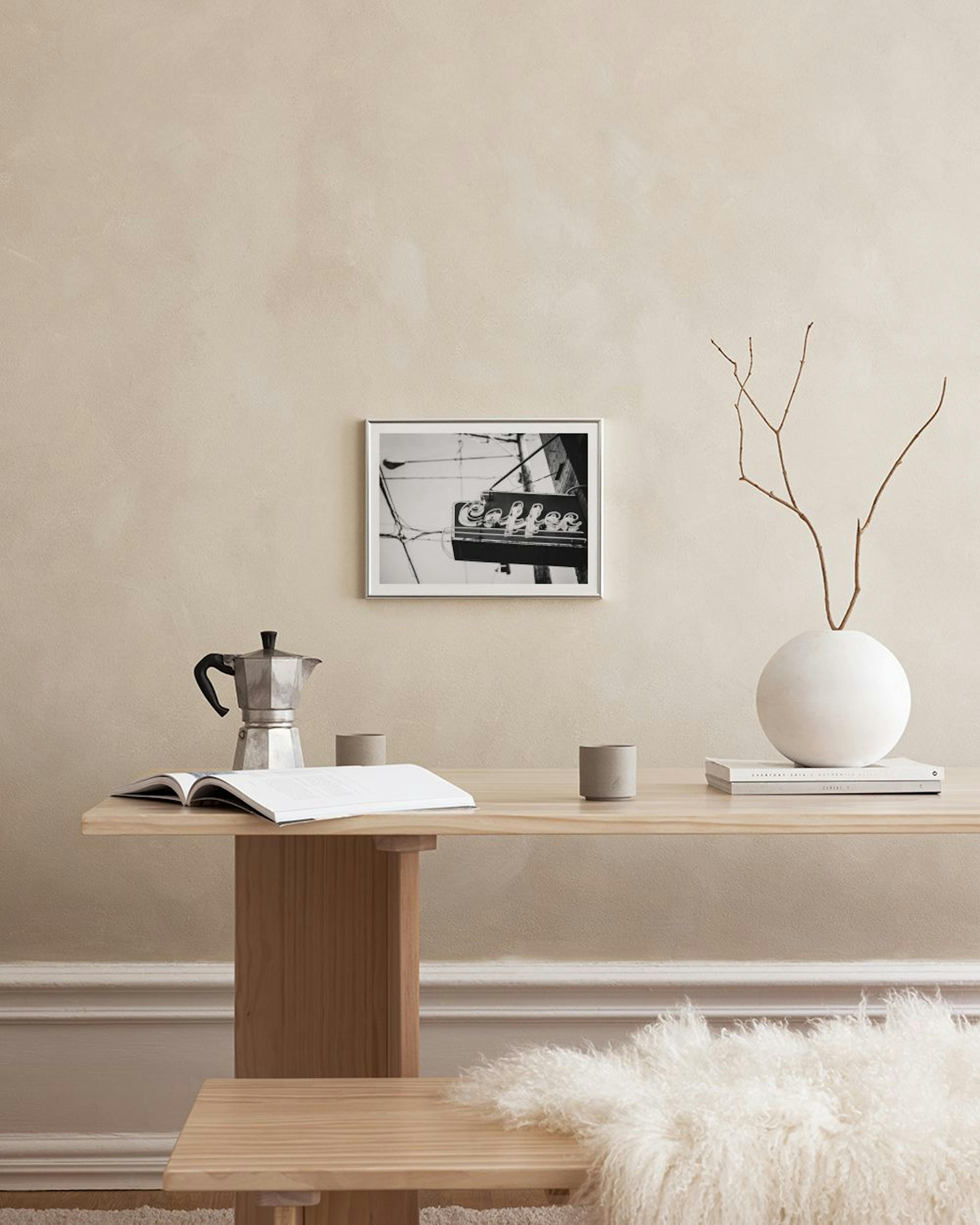 A black and white print of a neon “Coffee” sign, hanging above a white chest of drawers with decorative items.