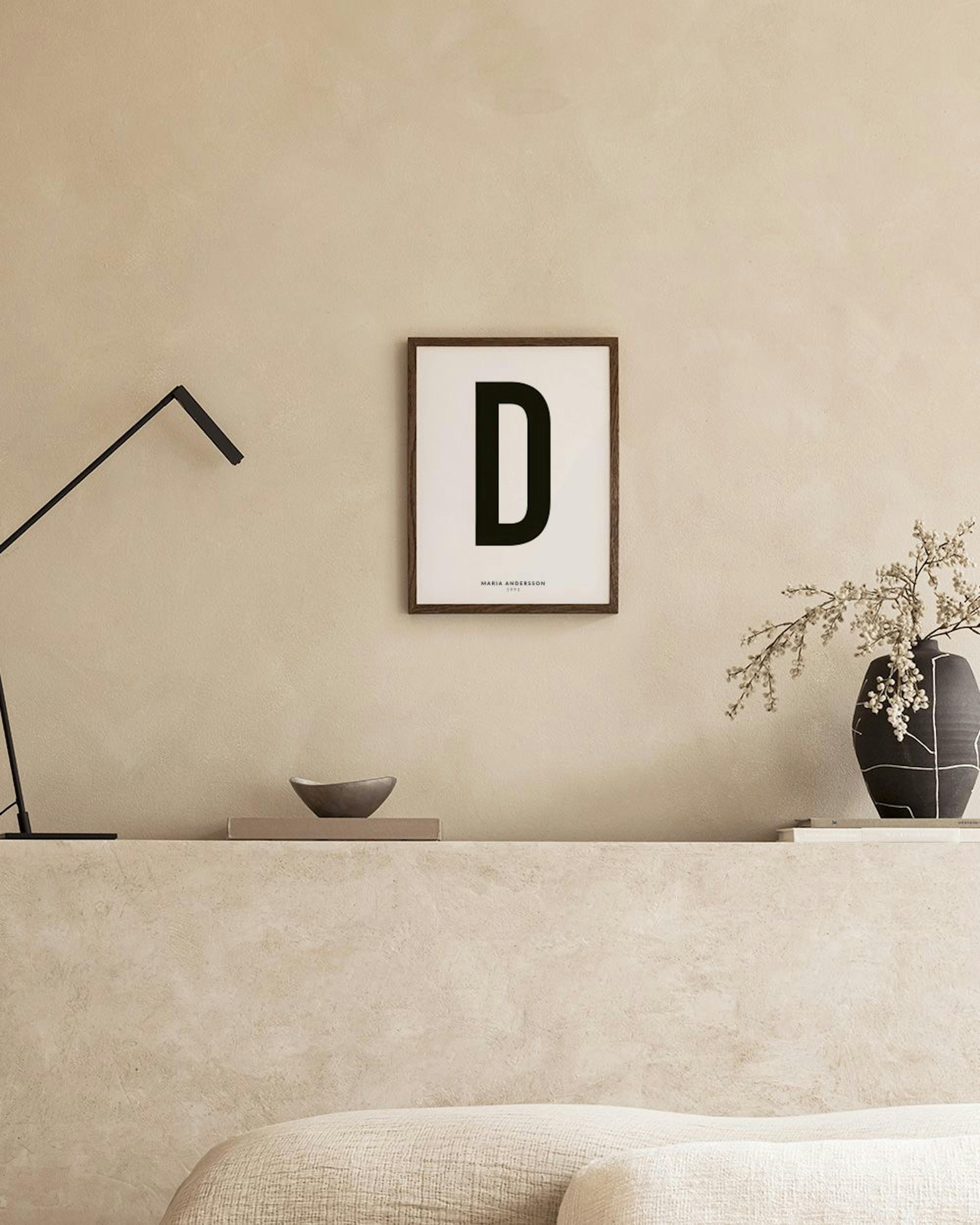 Ein personalisiertes Poster mit dem Buchstaben D und Namen, hängt über einem Nachttisch im Schlafzimmer.