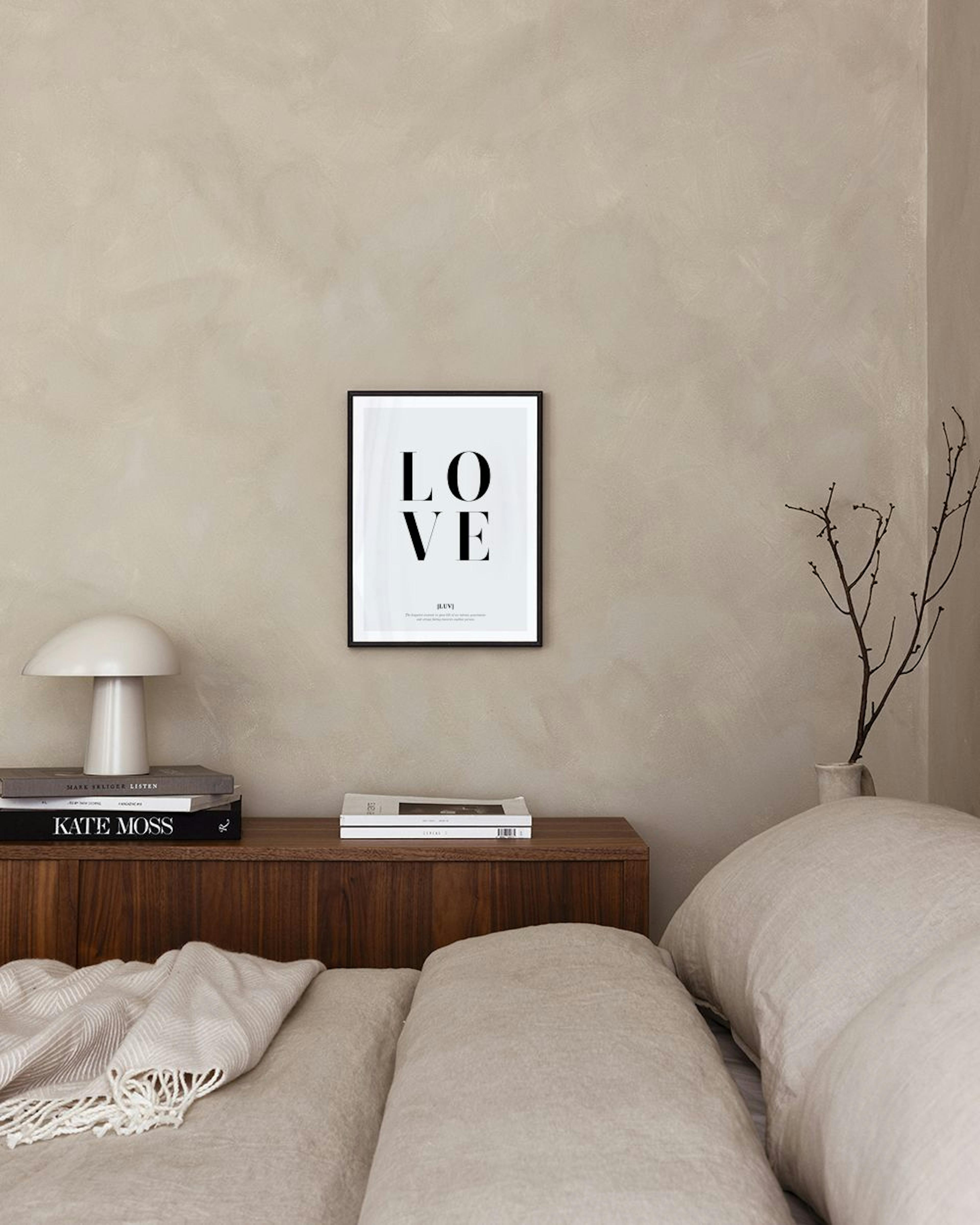 Poster med ordet LOVE i svarta versaler, text i svart, intill en kaktus och en guldljusstake på en vit hylla.