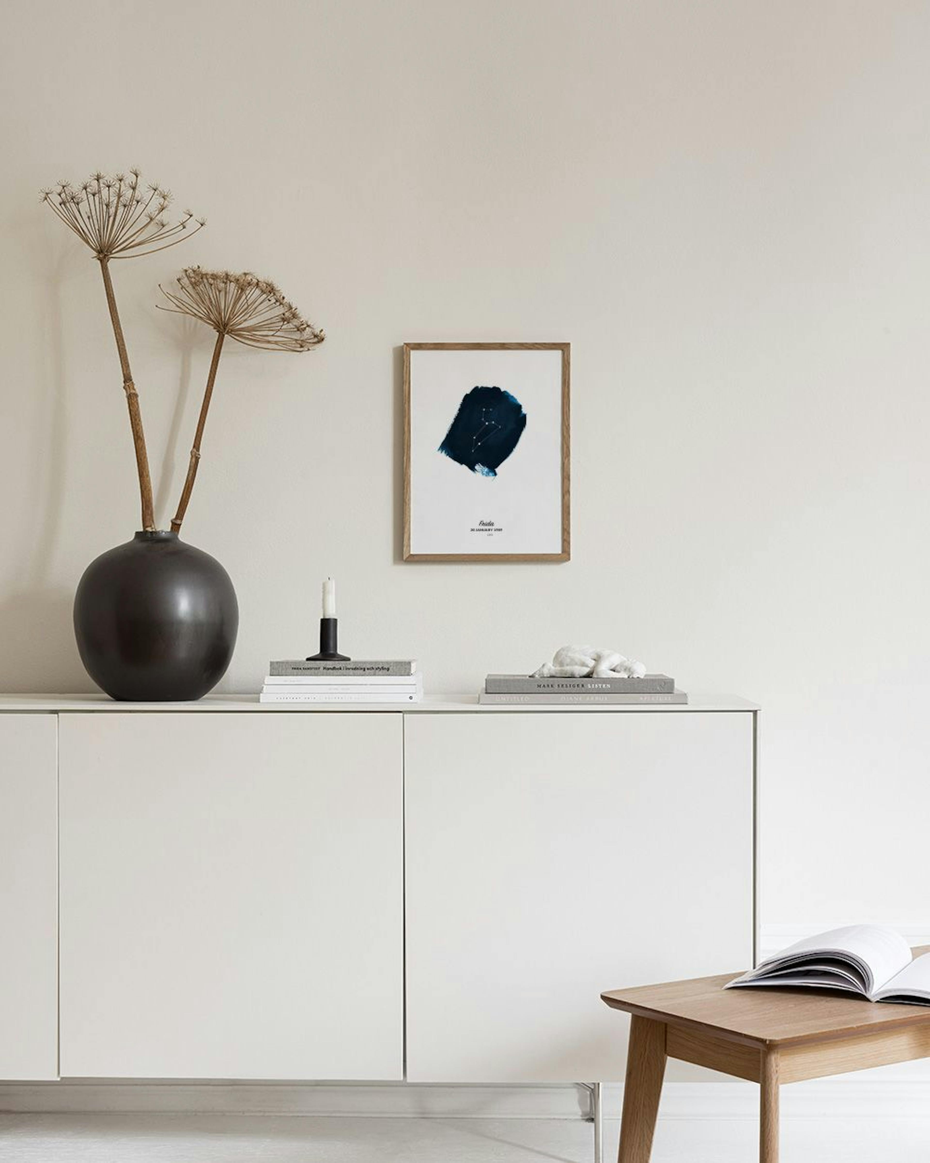 Affiche personnalisée avec constellation sur fond bleu marine, suspendue au-dessus dun meuble gris avec vases et livres.