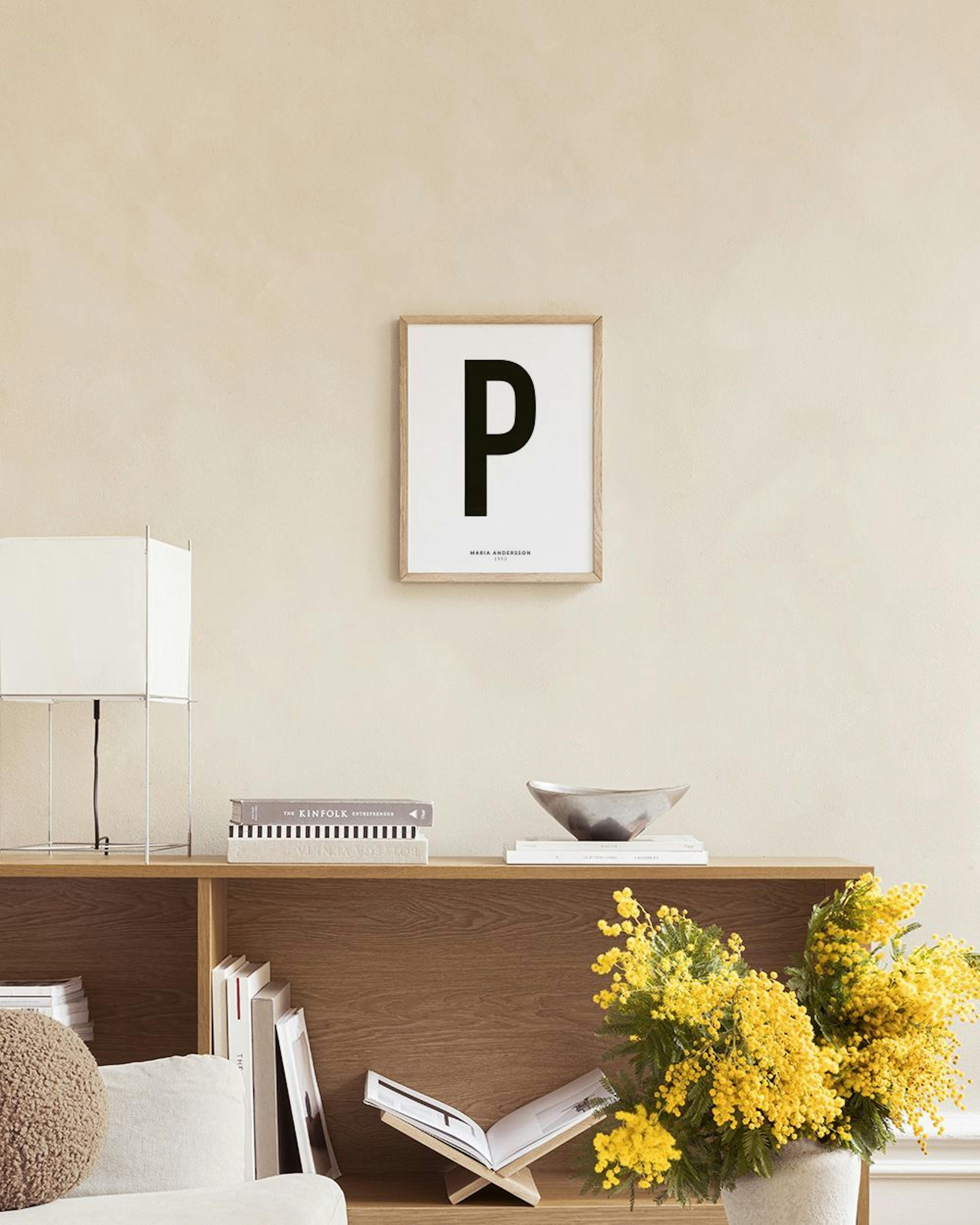 Poster personalizado com a letra P a preto, em fundo branco, exibido num móvel cinzento com livros e objetos decorativos.