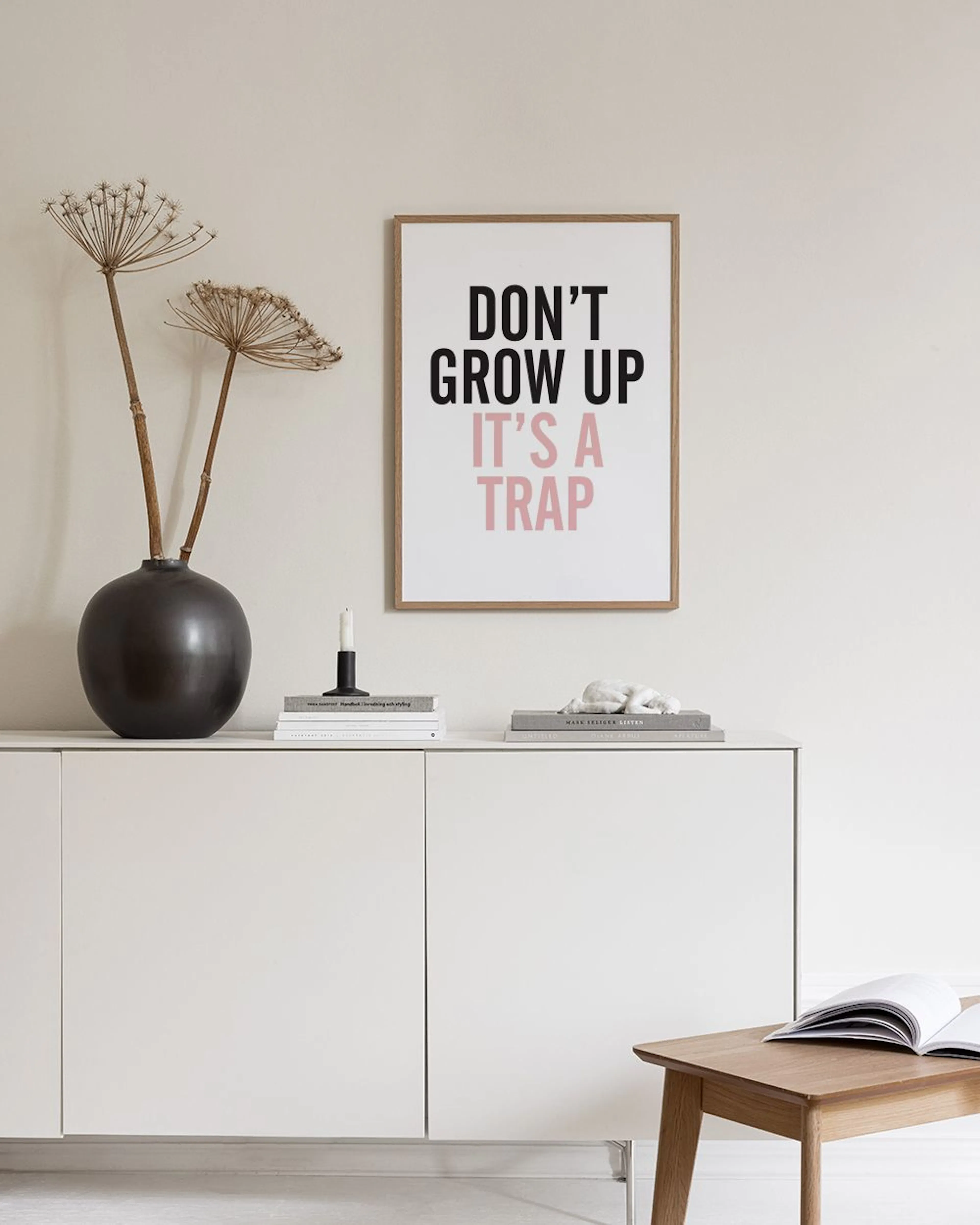 Affiche sur un bureau blanc avec les mots DONT GROW UP ITS A TRAP, près dune lampe blanche et dobjets dorés.