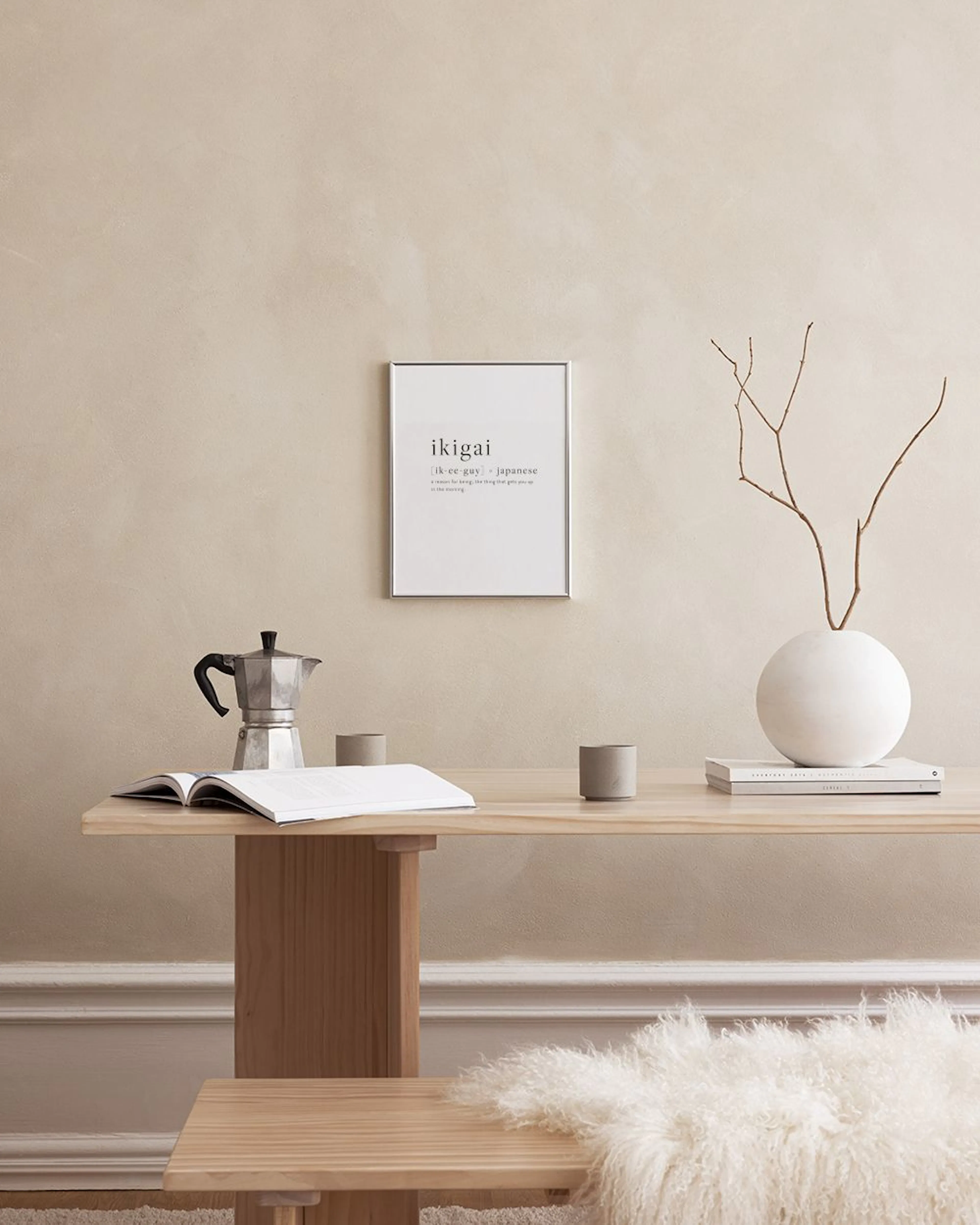 A minimalist print defining ikigai in Japanese, hanging above a bed with grey bedding and a black bedside table.