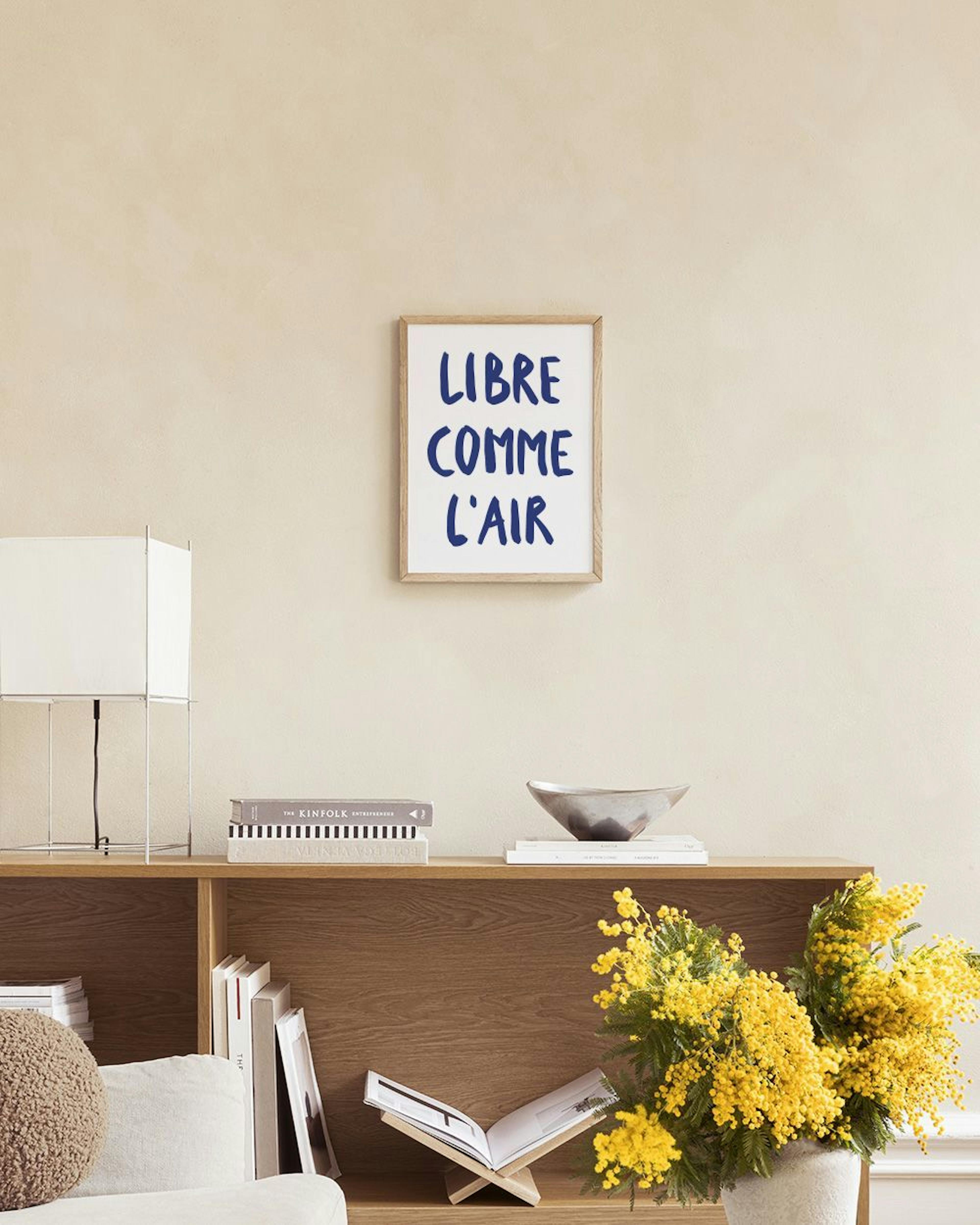 A print with blue handwritten French text Libre Comme LAir on a white background, hanging above a white cabinet with decorative 