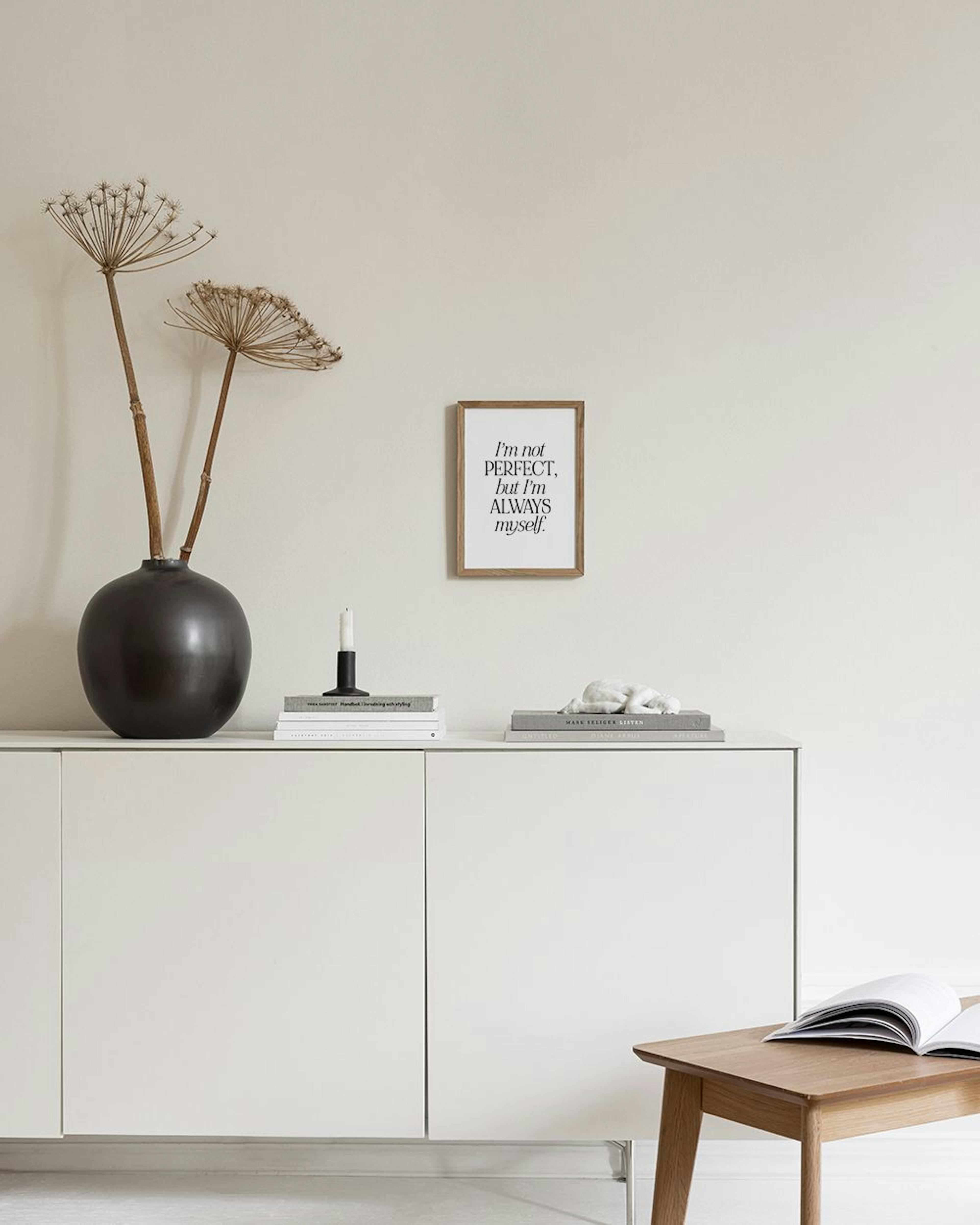 A motivational print with the text “I’m not perfect, but I’m always myself.” displayed on a white dresser with flowers and candl