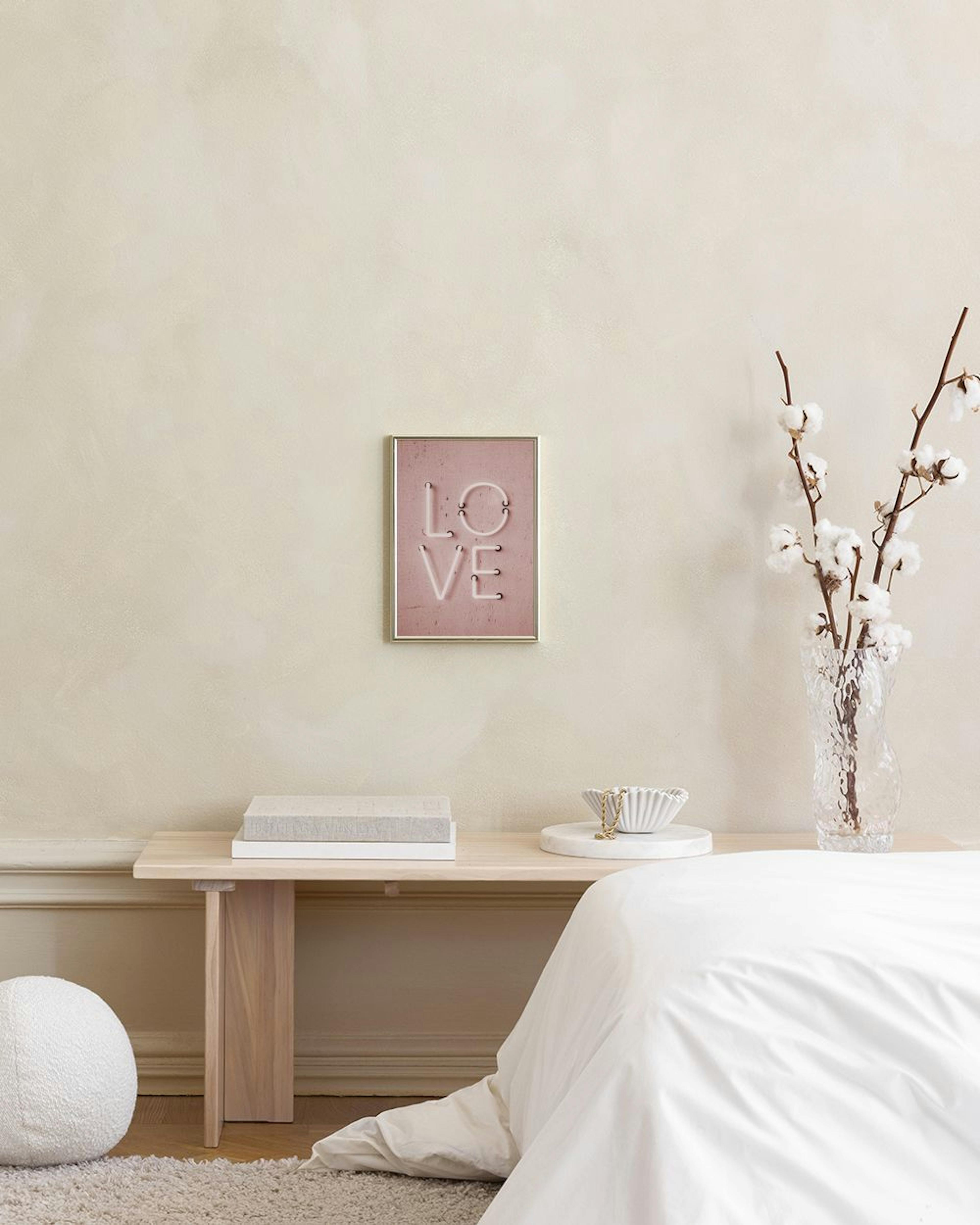 A print of the word LOVE in white neon letters on a pink concrete background, displayed above a white cabinet with a lamp and bo