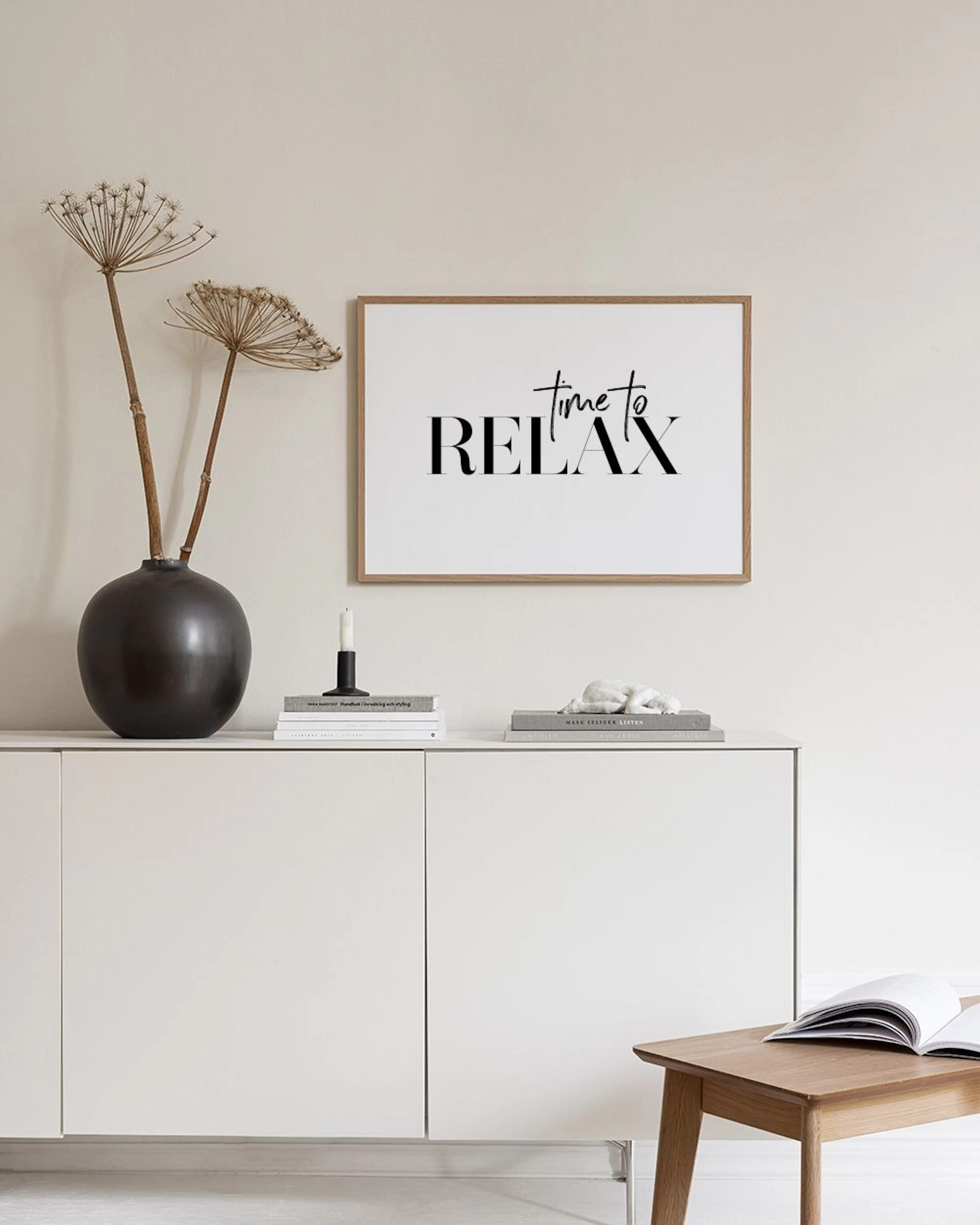 Plakat z napisem time to RELAX w czerni, wiszący nad czarną konsolą z książkami i klepsydrami w nowoczesnym wnętrzu.