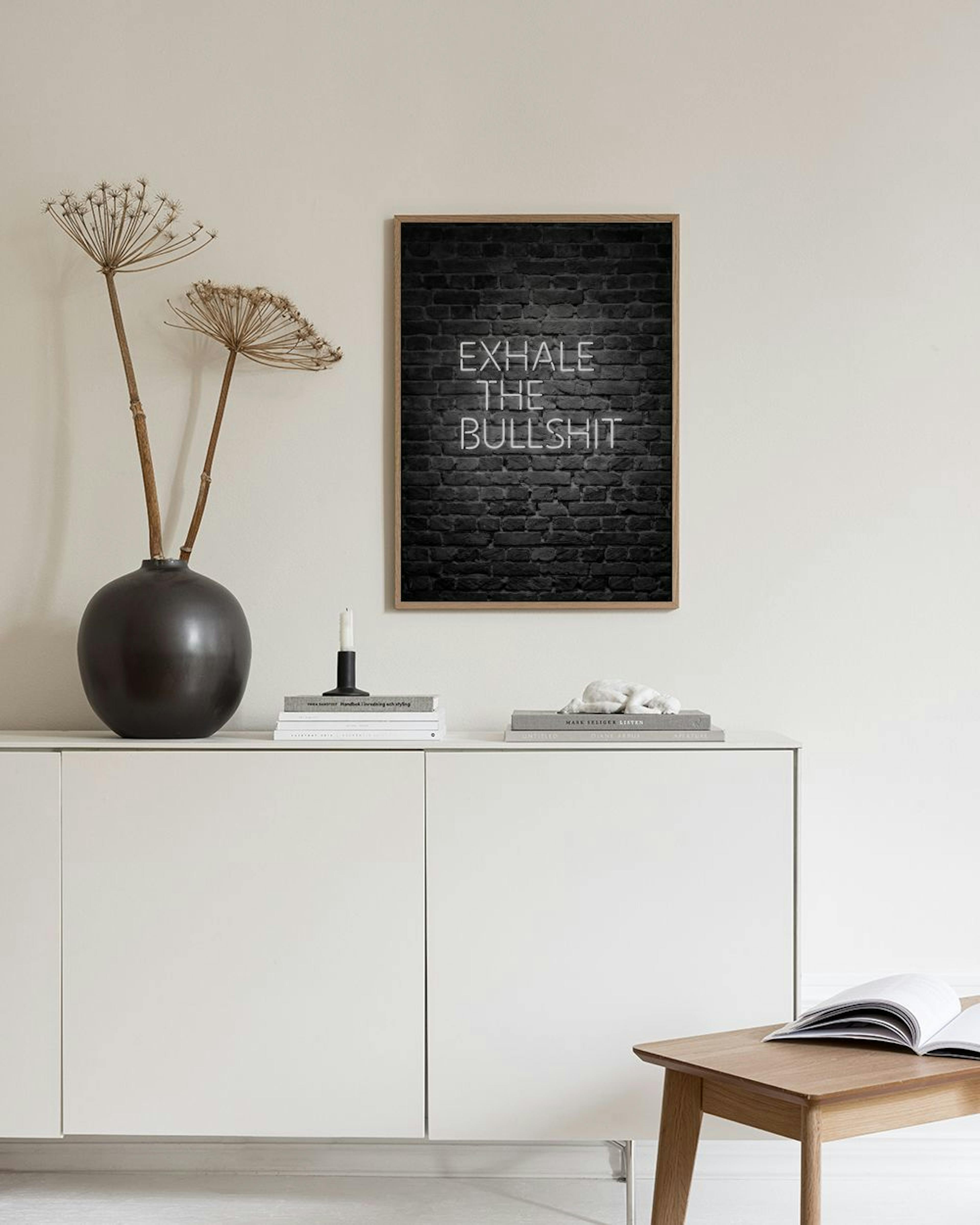 A print with white neon text EXHALE THE BULLSHIT on a dark brick wall background, displayed in a room with two grey pedestals an