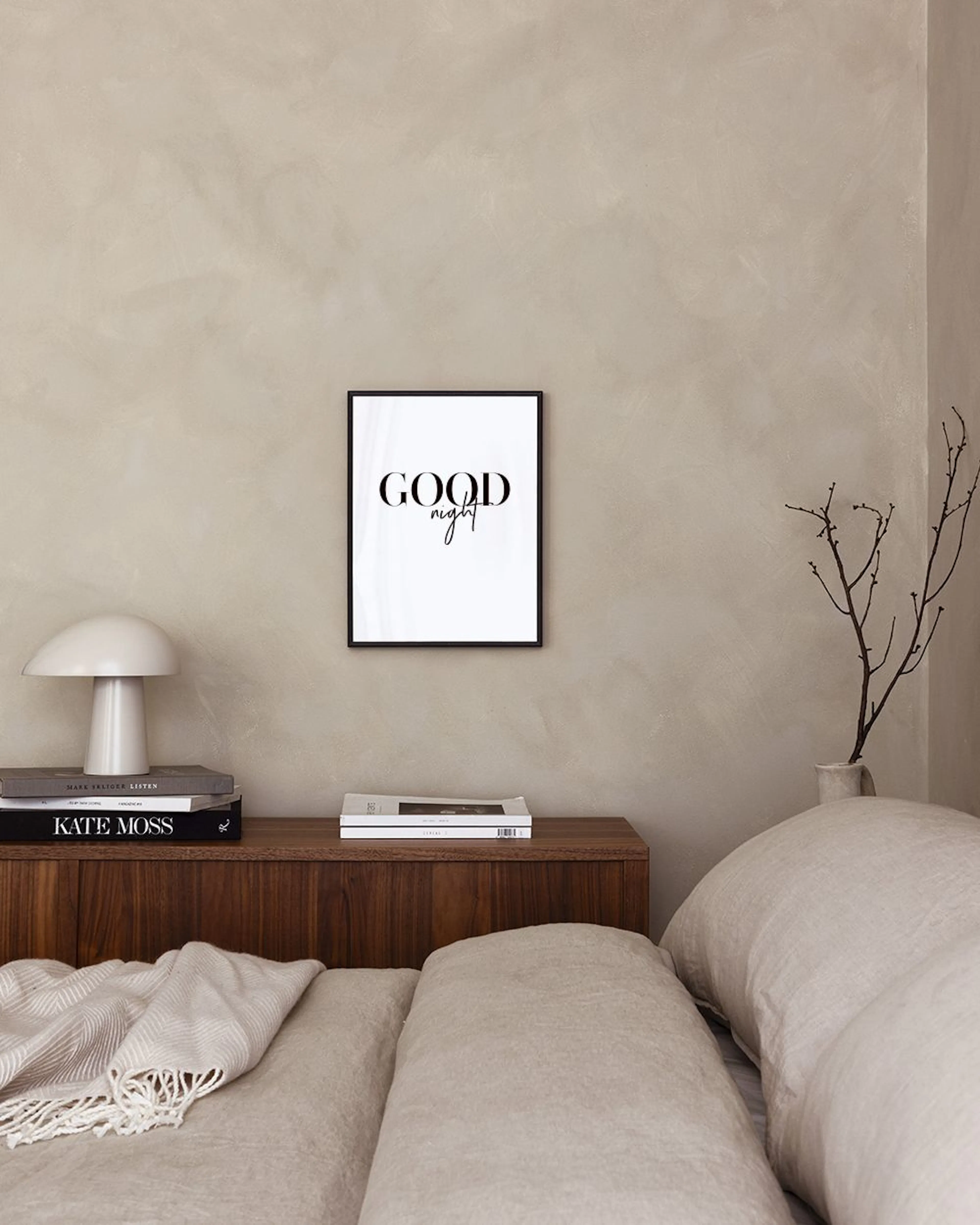 A minimalist print with GOOD in bold serif and night in script font, hanging above books and decor on a black surface.