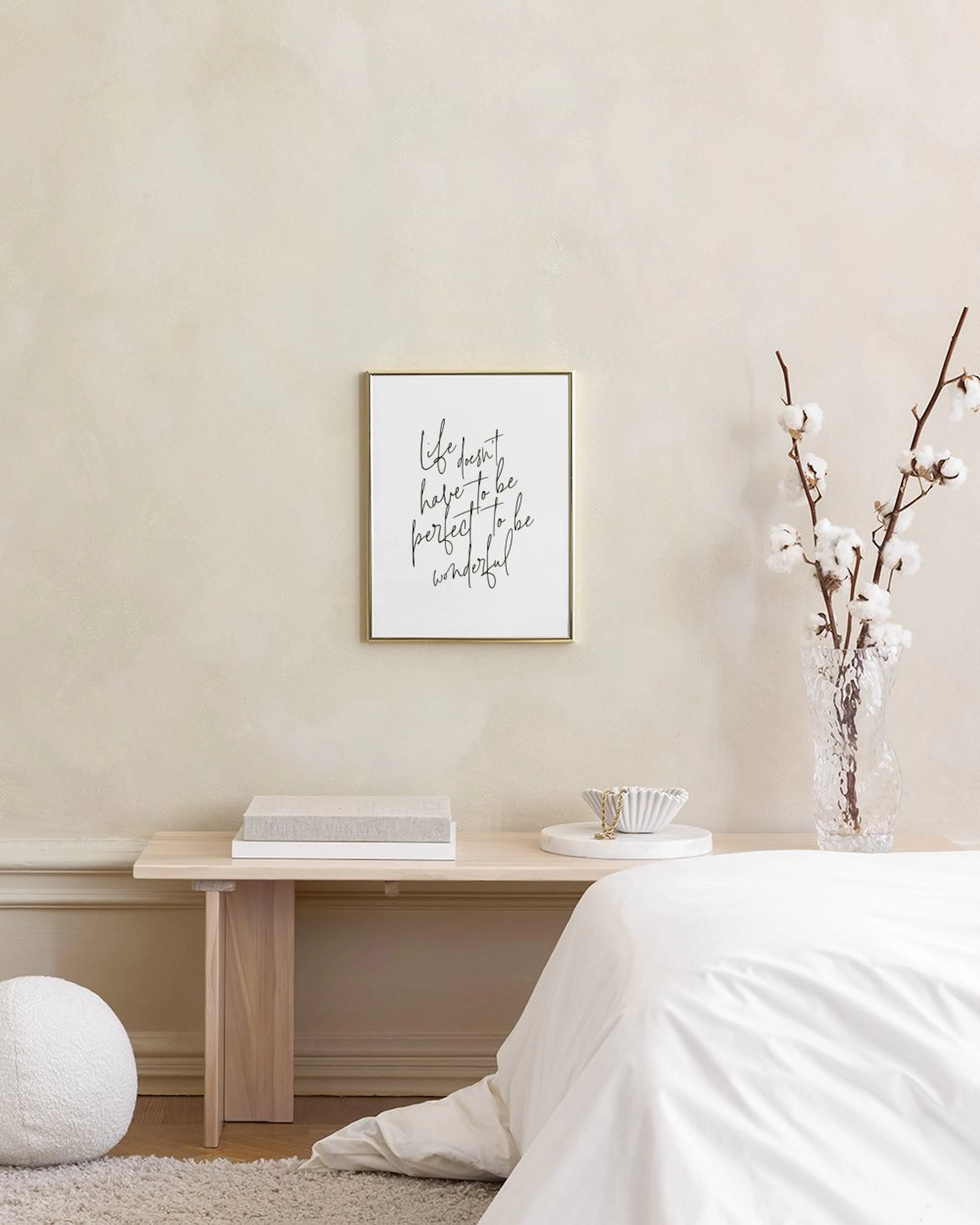 Affiche murale avec citation calligraphiée noire sur fond blanc, au-dessus dun meuble blanc avec vase et plante.