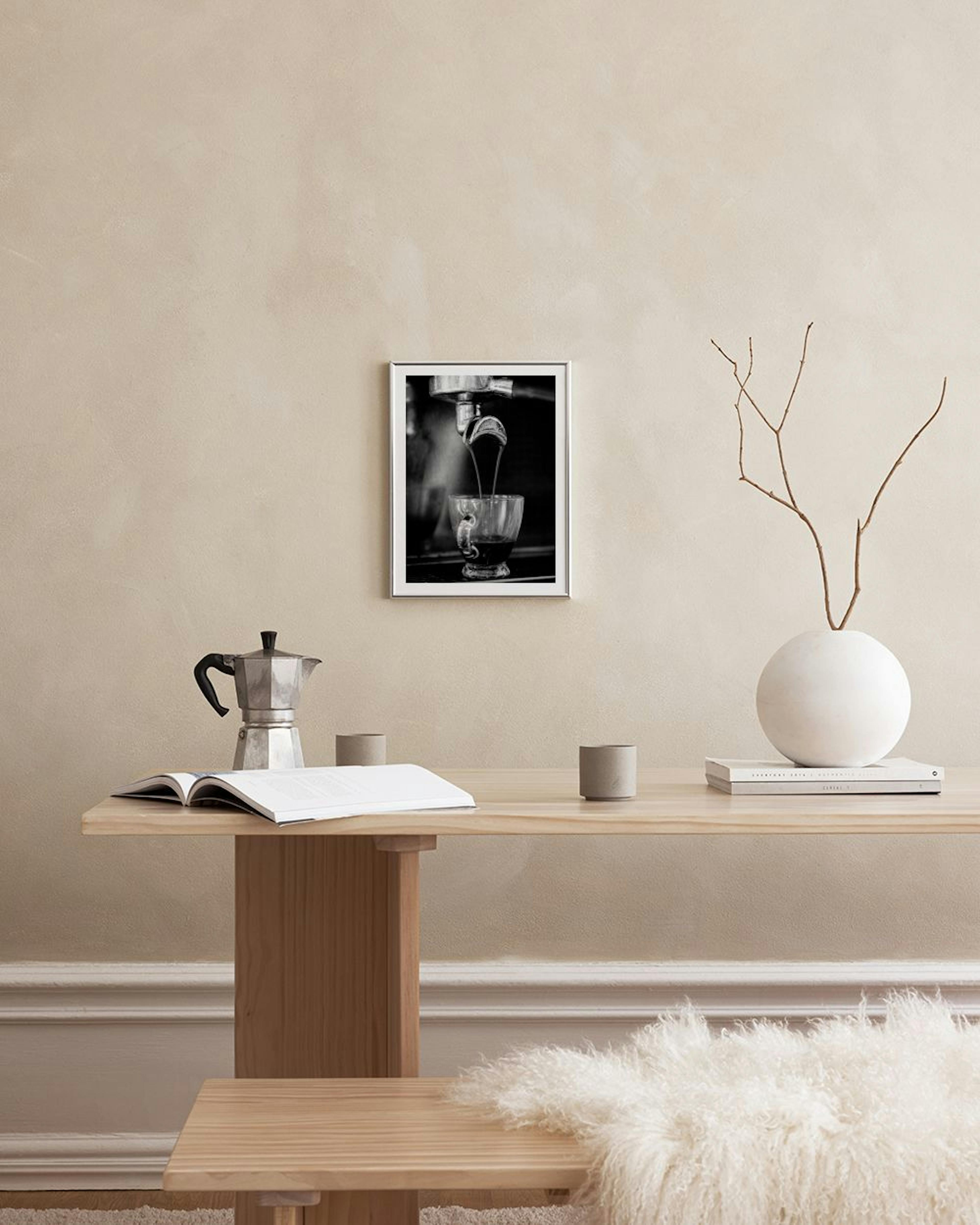 Schwarz-weiß Poster einer Kaffeemaschine, die Espresso in eine Tasse laufen lässt, an einer Wand über einem Esstisch.