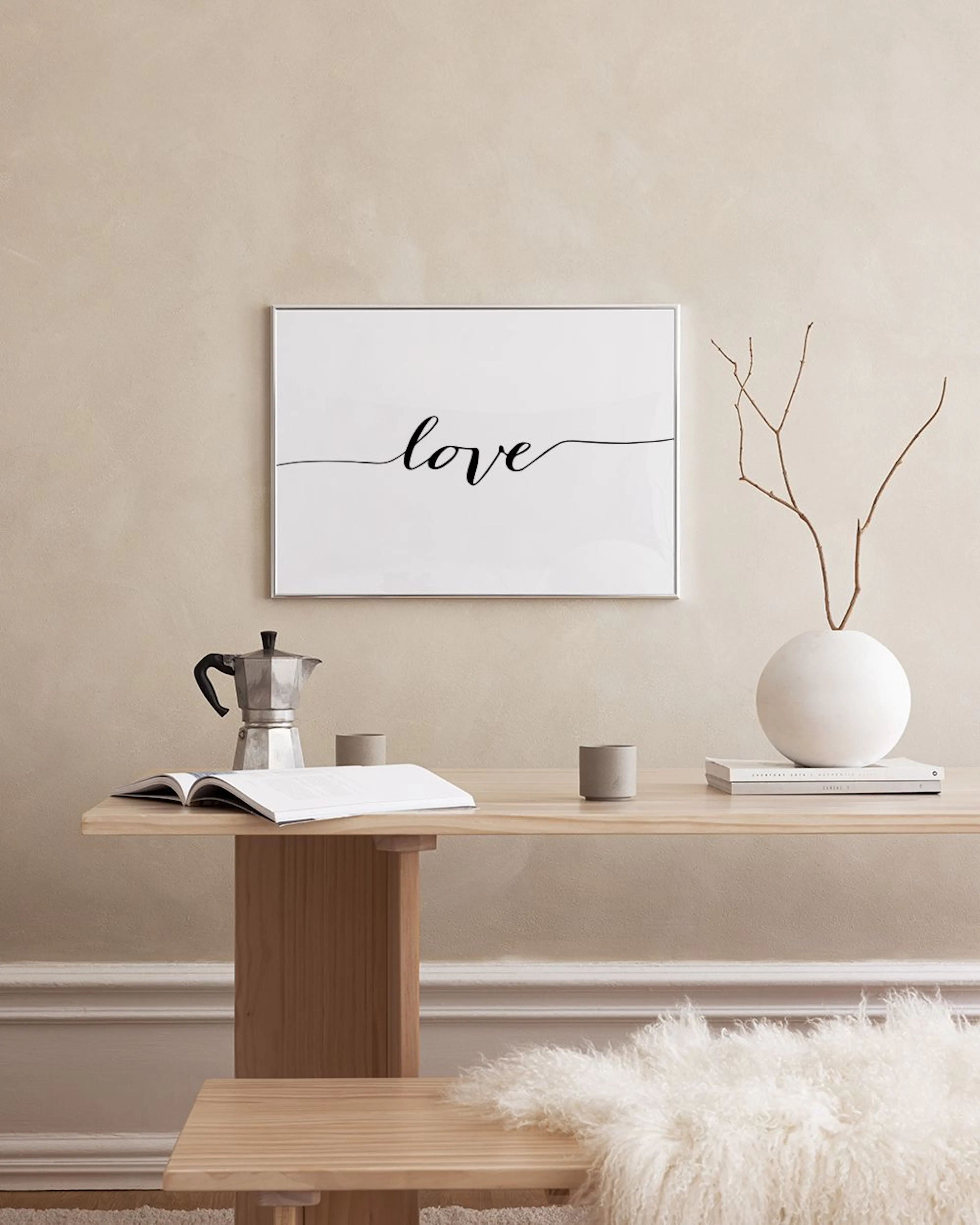 A print with the word love in script on a white background, hanging in a bright living room above a white sofa.