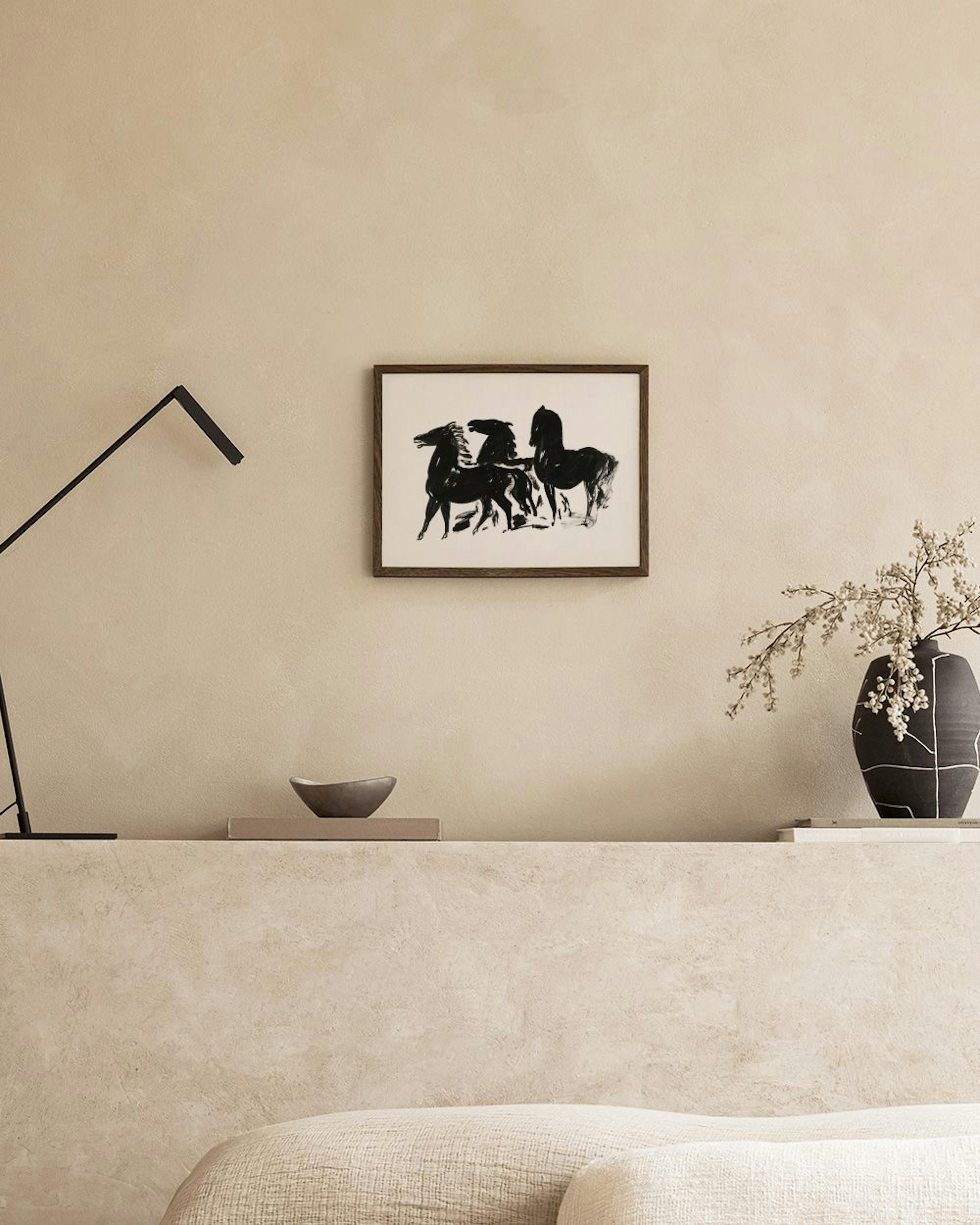 Affiche dart de trois chevaux noirs stylisés, suspendue au-dessus dun lit avec une literie blanche et un livre ouvert.