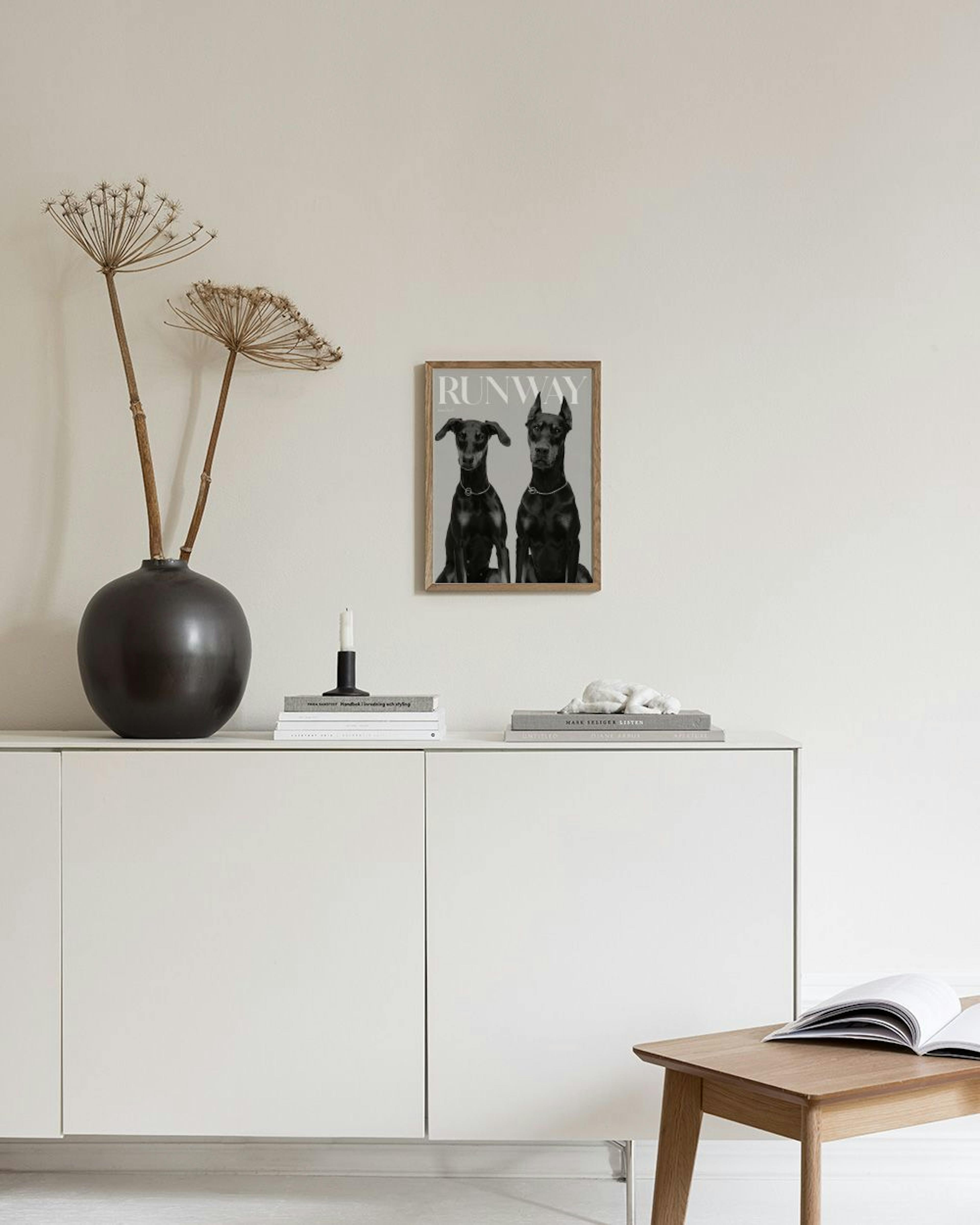 Een poster met zwart-wit foto van twee elegante Dobermanns met halsbanden, RUNWAY erboven, hangend in een lichte woonkamer boven