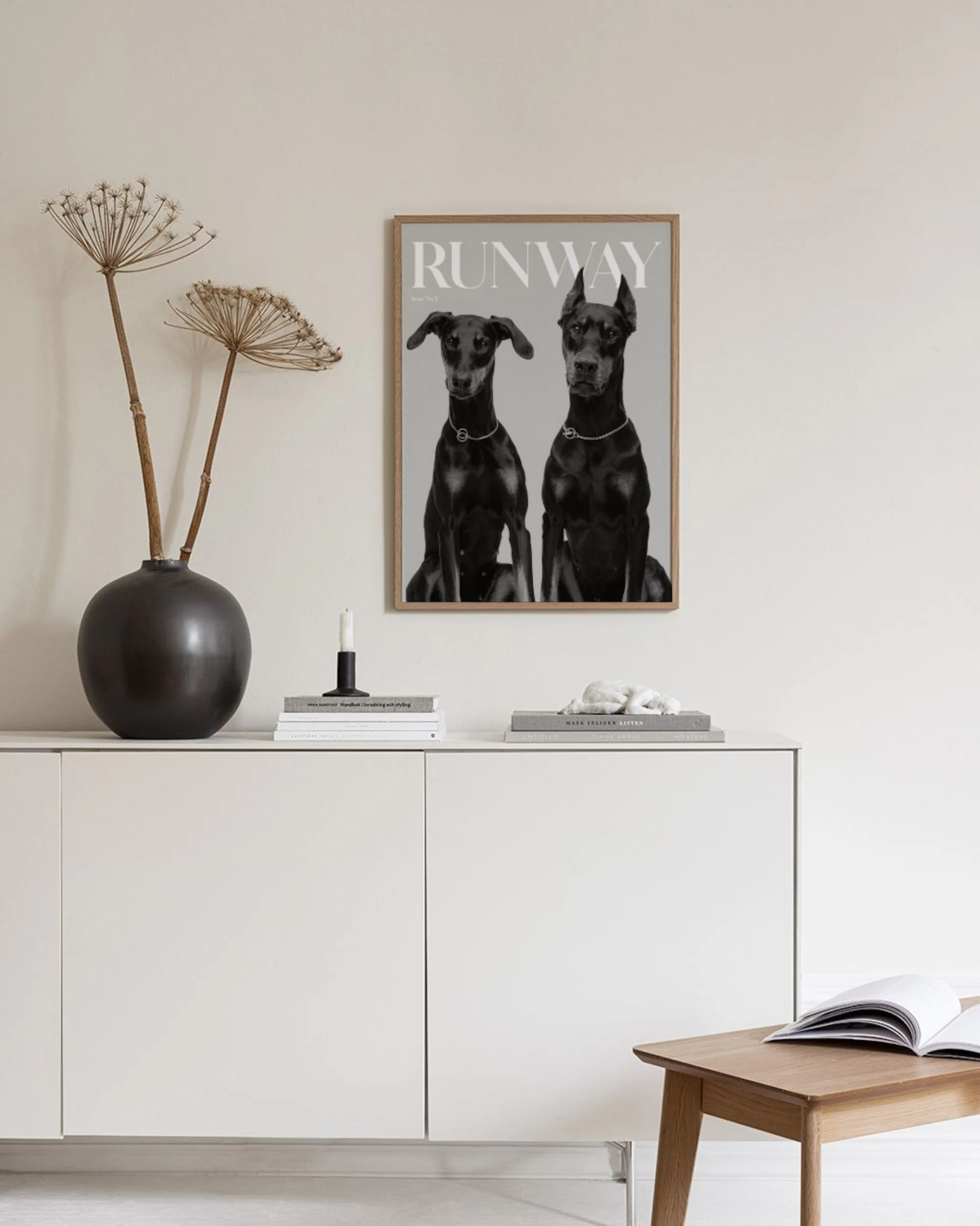 A black and white print of two Doberman dogs with RUNWAY text, hanging in a living room above a cream sofa.