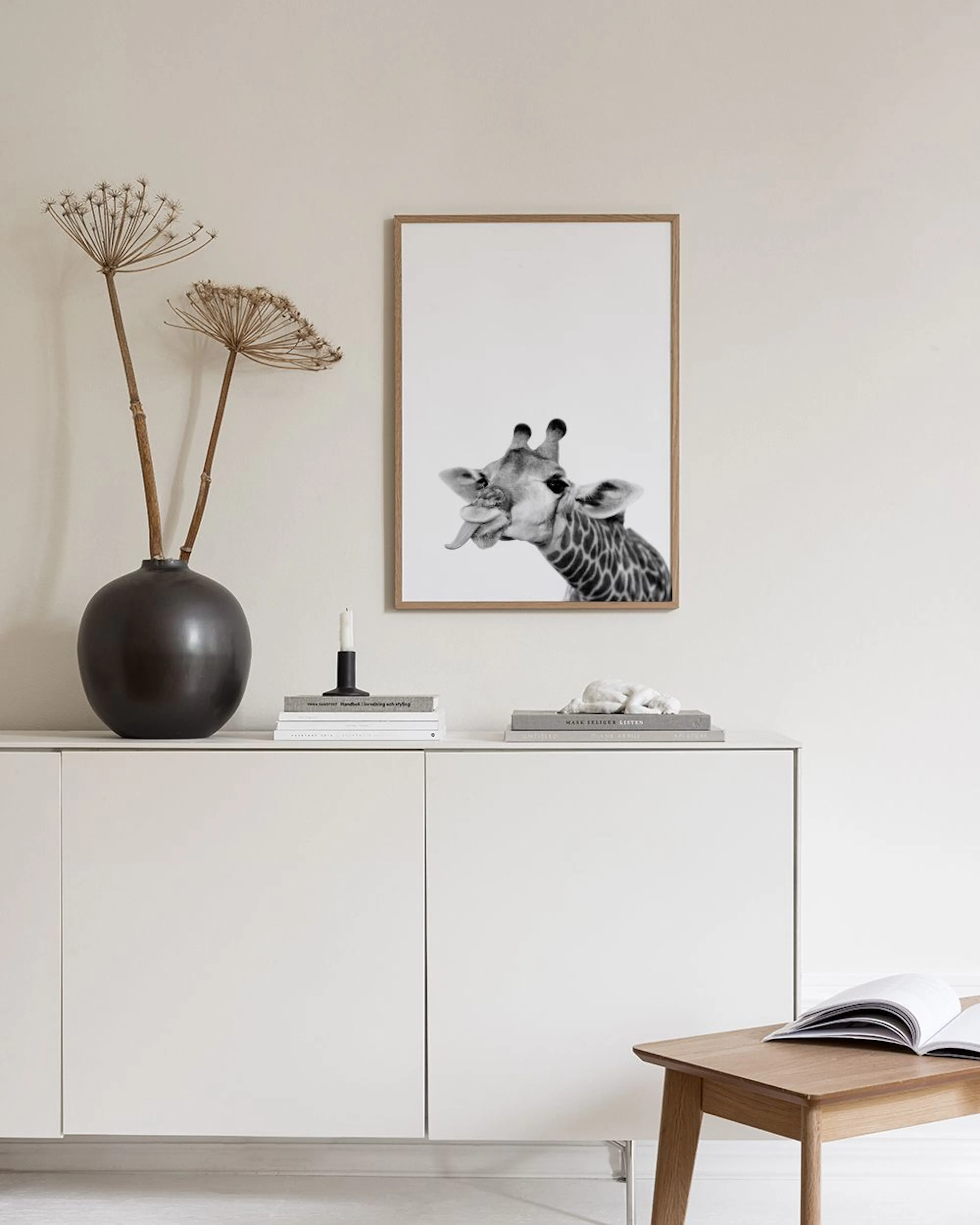 A black and white print of a giraffe with its tongue out, displayed above a white cabinet with decor.