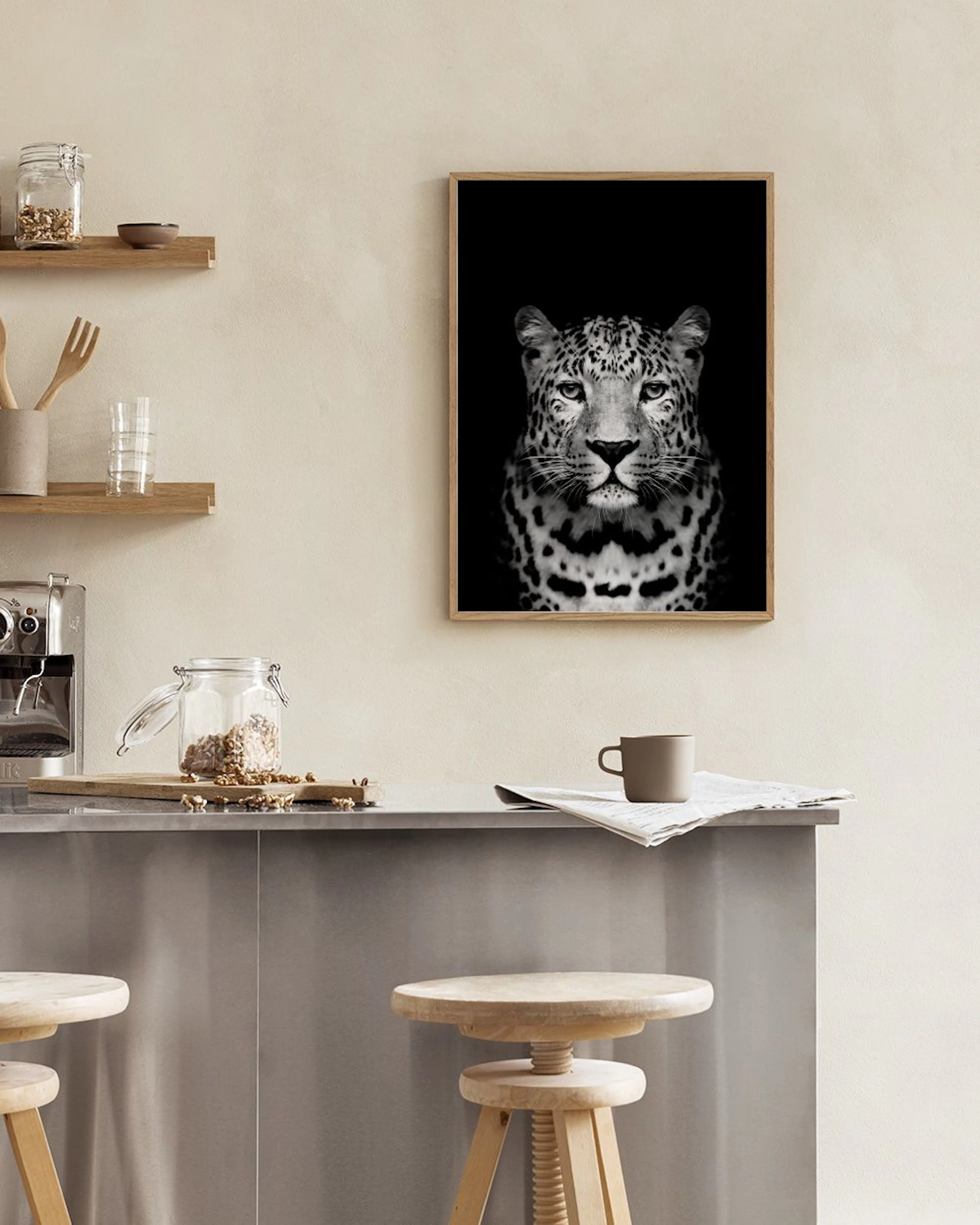 Plakat med portræt af en leopard i sort og hvid, hængende på en mørkeblå væg over en mørkeblå puf med gylden base.