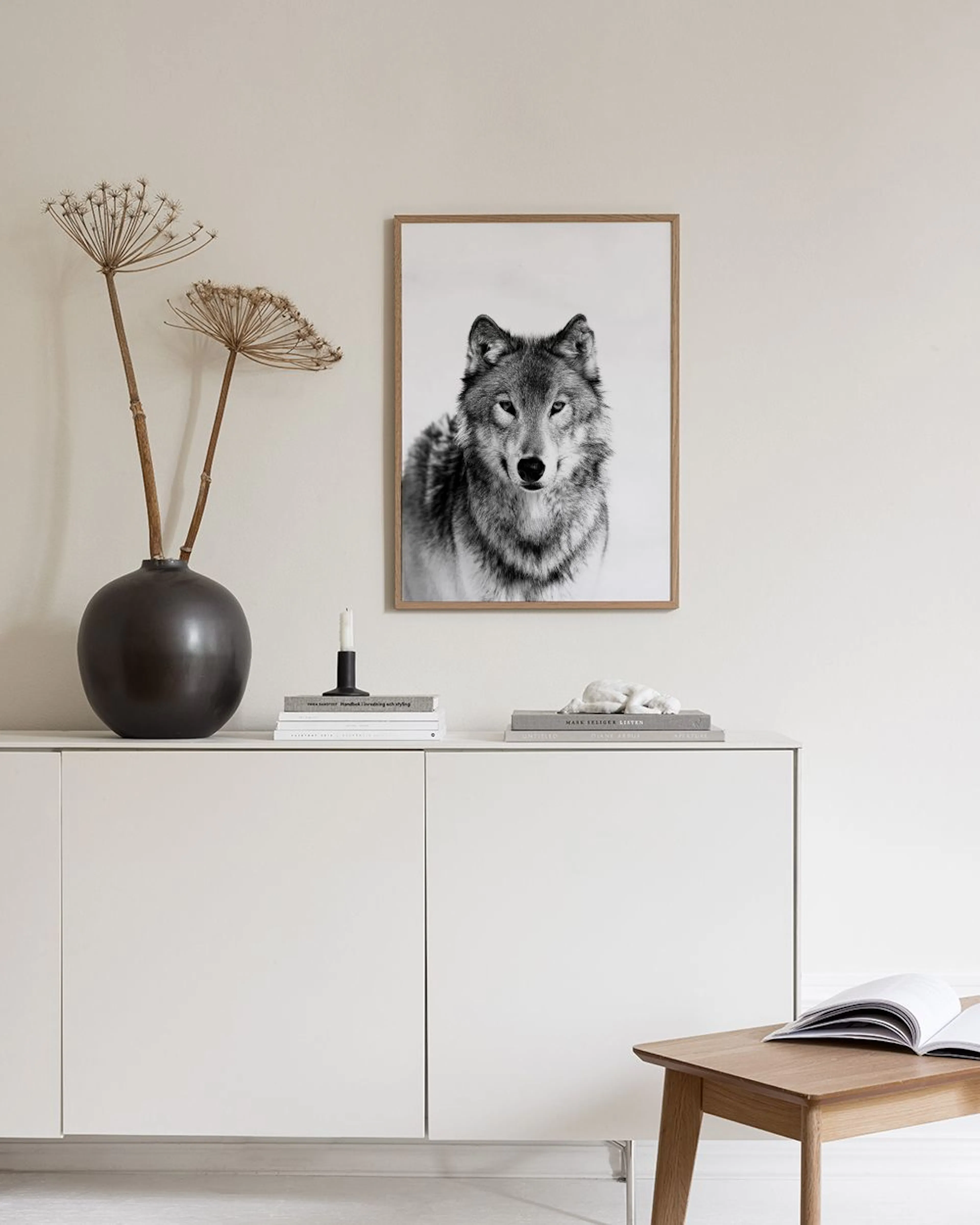 Poster van een grijze wolf met intense ogen, hangend boven een krukje met boeken in een lichte hal.