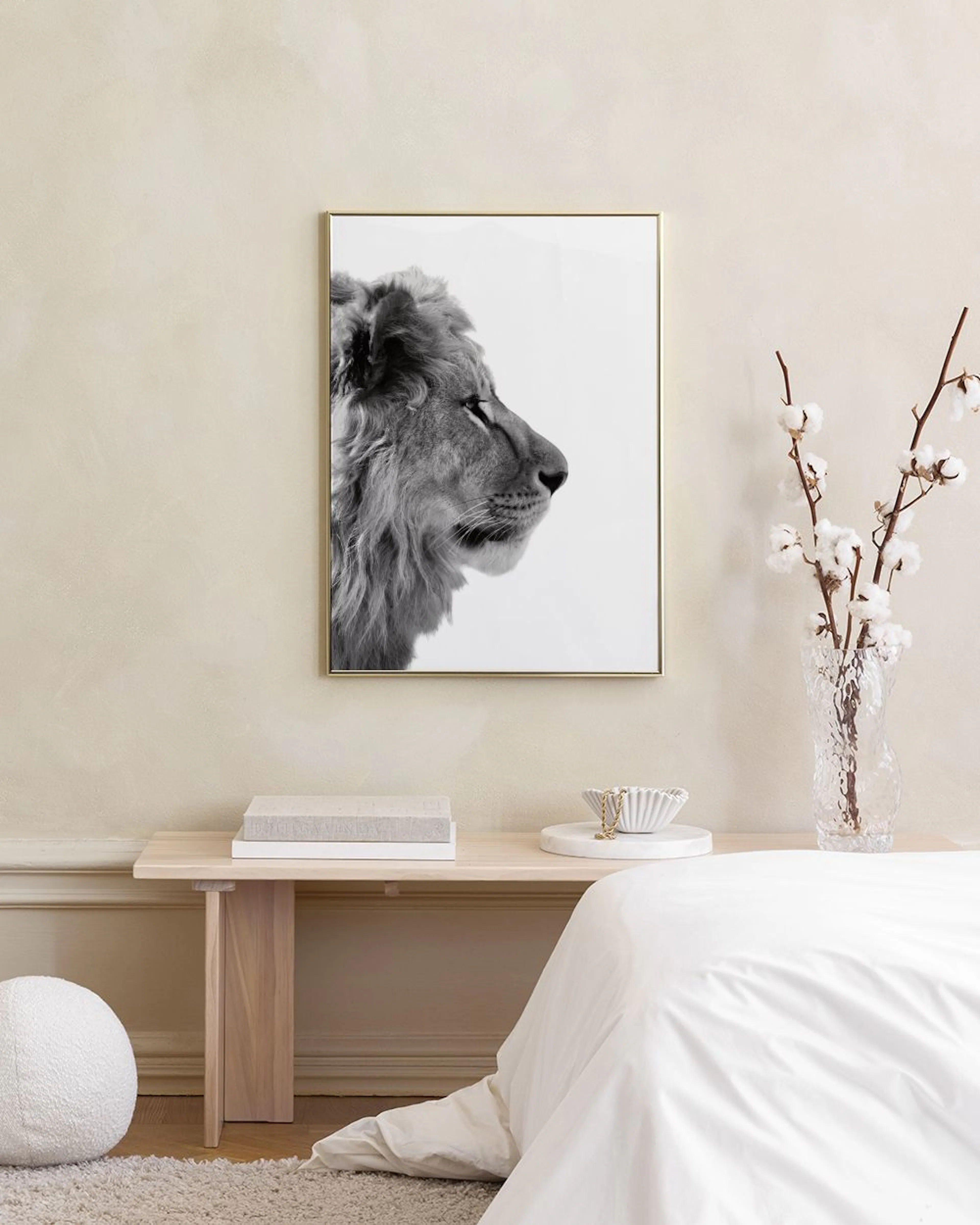 A black and white print of a lions head in profile hanging on a grey wall in a living room with a pink ottoman and white sofa.