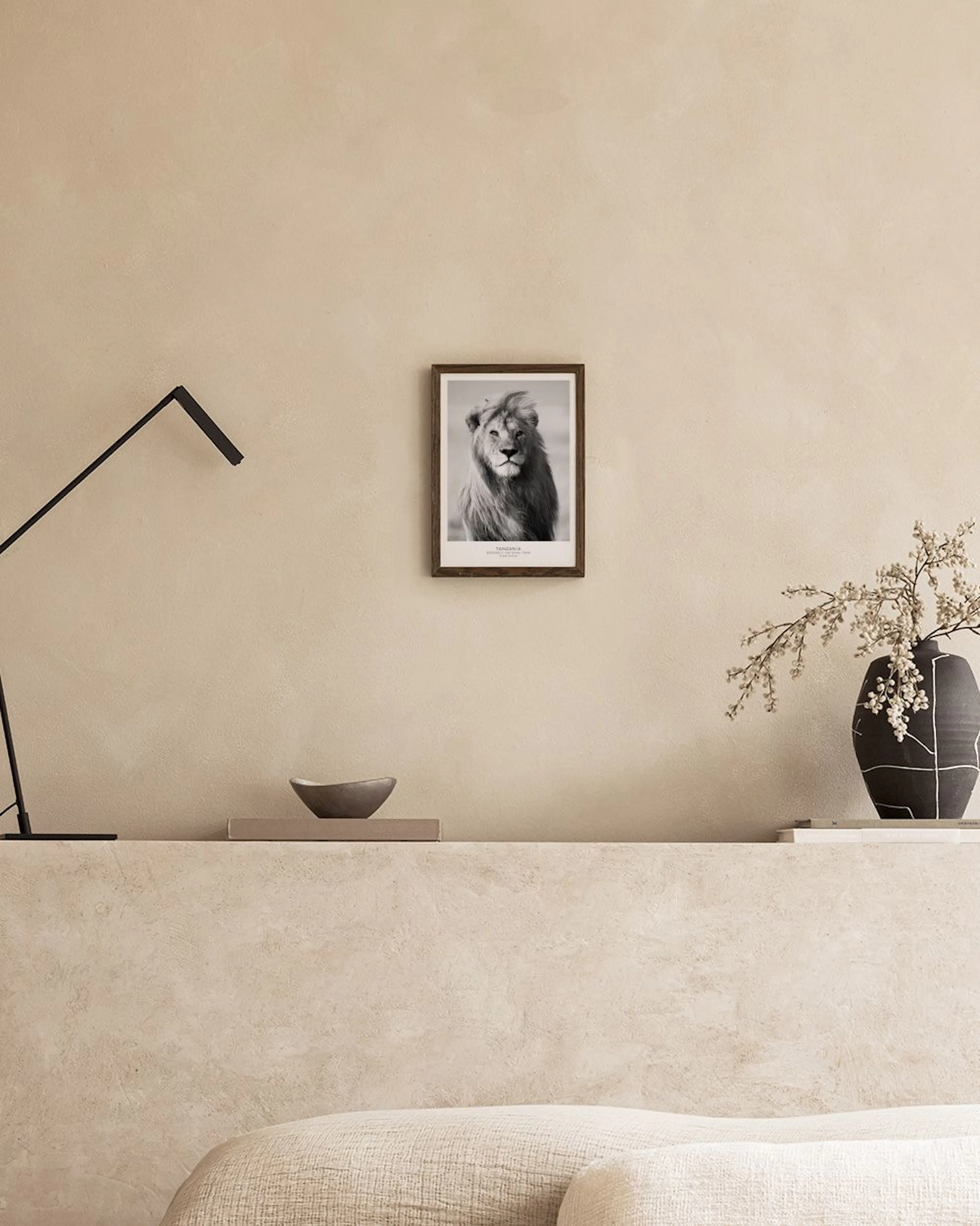 Black and white print of a lions head with a flowing mane, hanging on a black grid above two vases and a table lamp.