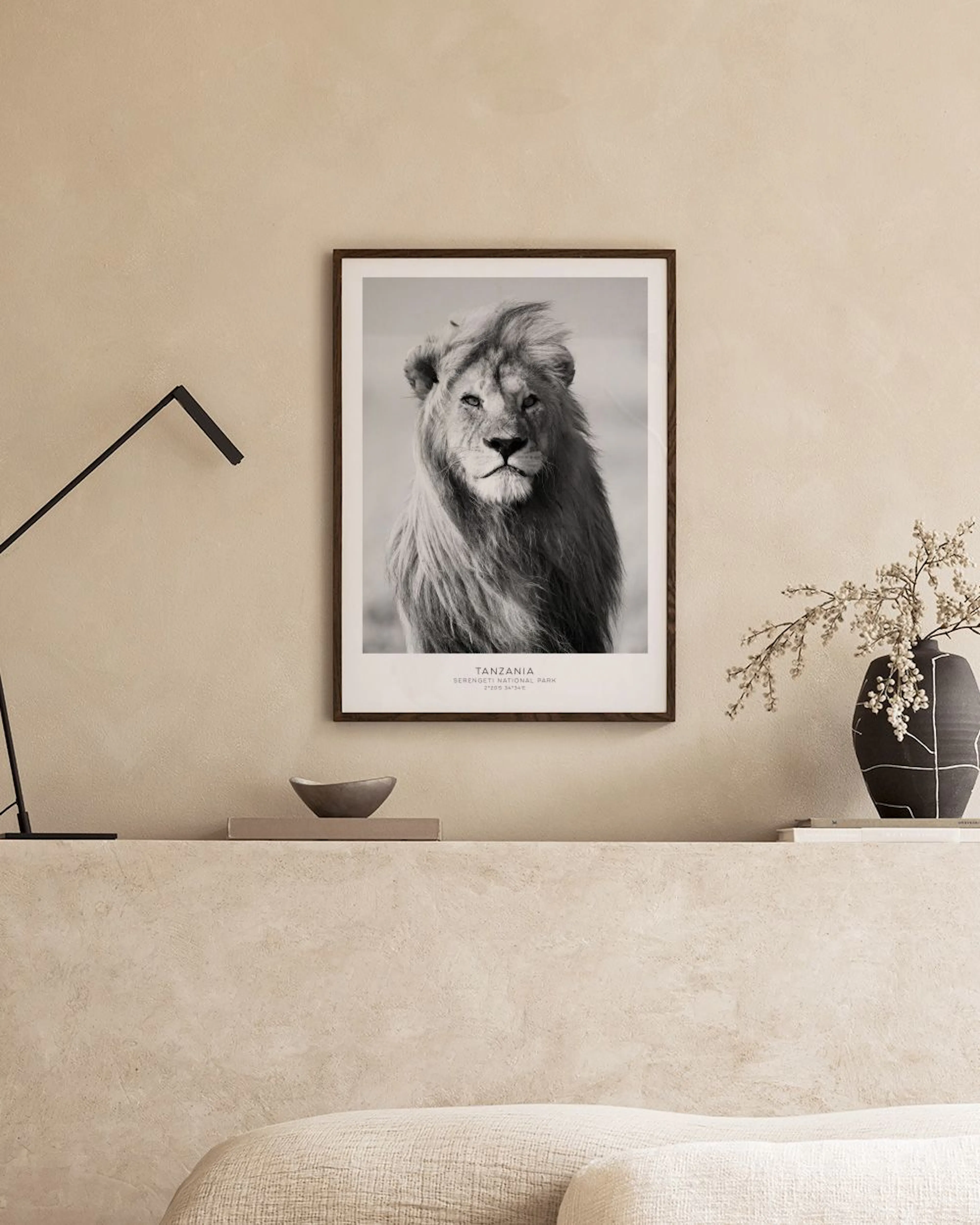 Sort-hvid plakat af en løve med manke, hængende på en sort gittervæg i et minimalistisk rum med to vaser og en lampe.