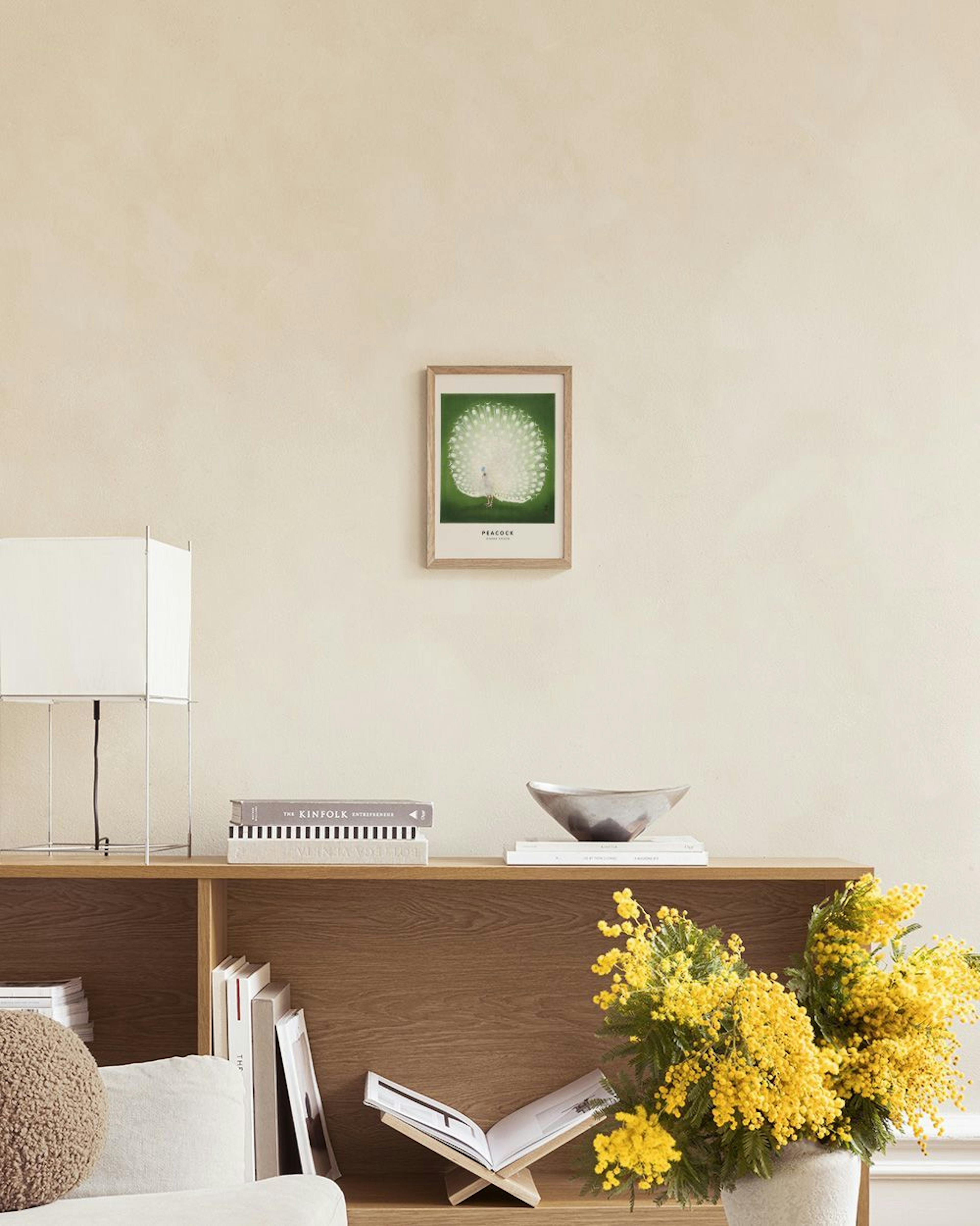 A print of a white peacock with tail feathers fanned out on a green background, displayed above a white cabinet with decorative 