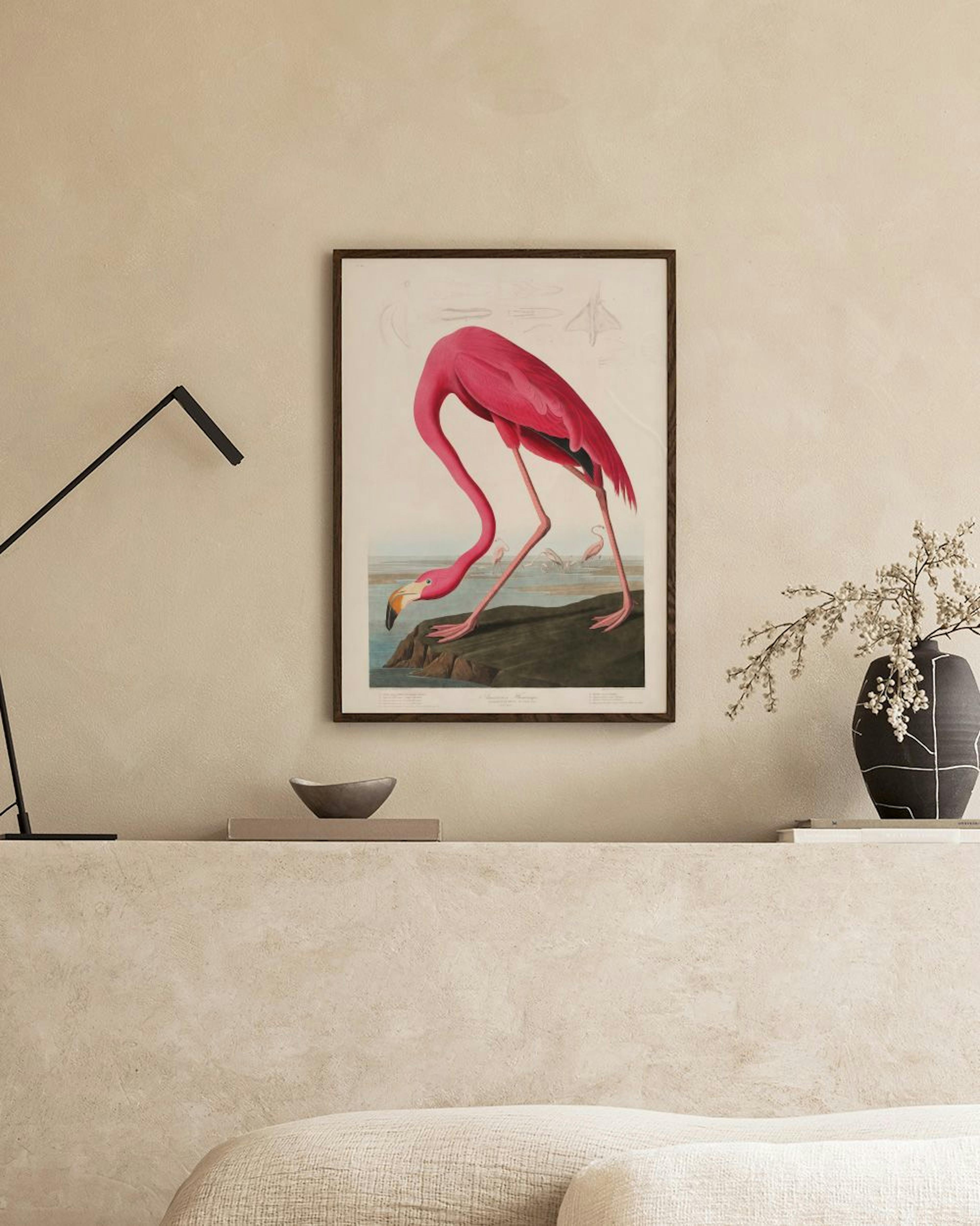 A print of a pink flamingo bending to drink from water, displayed above a black console table with decorative items.