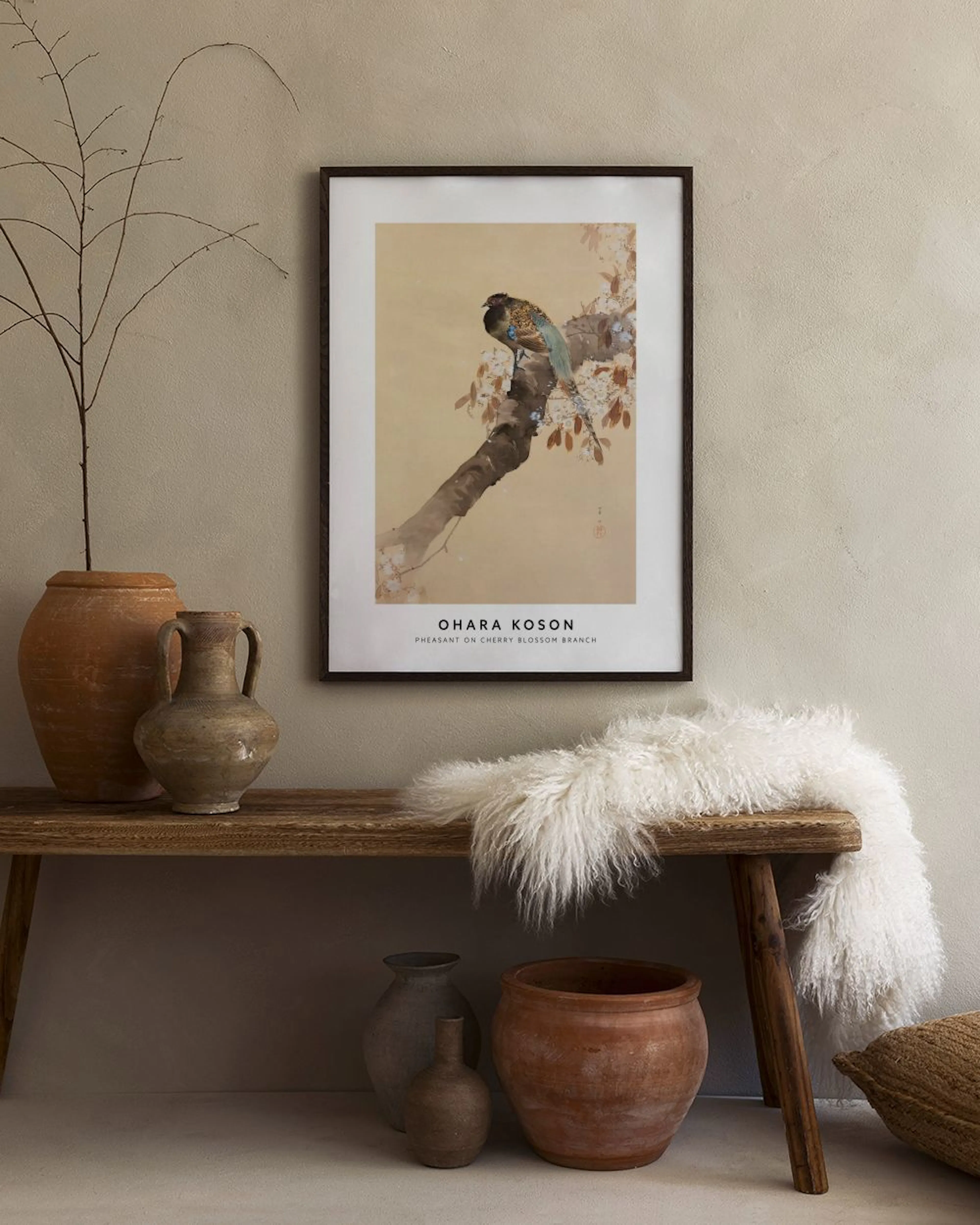 A print of a colorful pheasant perched on a cherry blossom branch, hanging above a wooden cabinet with decorative vases and book