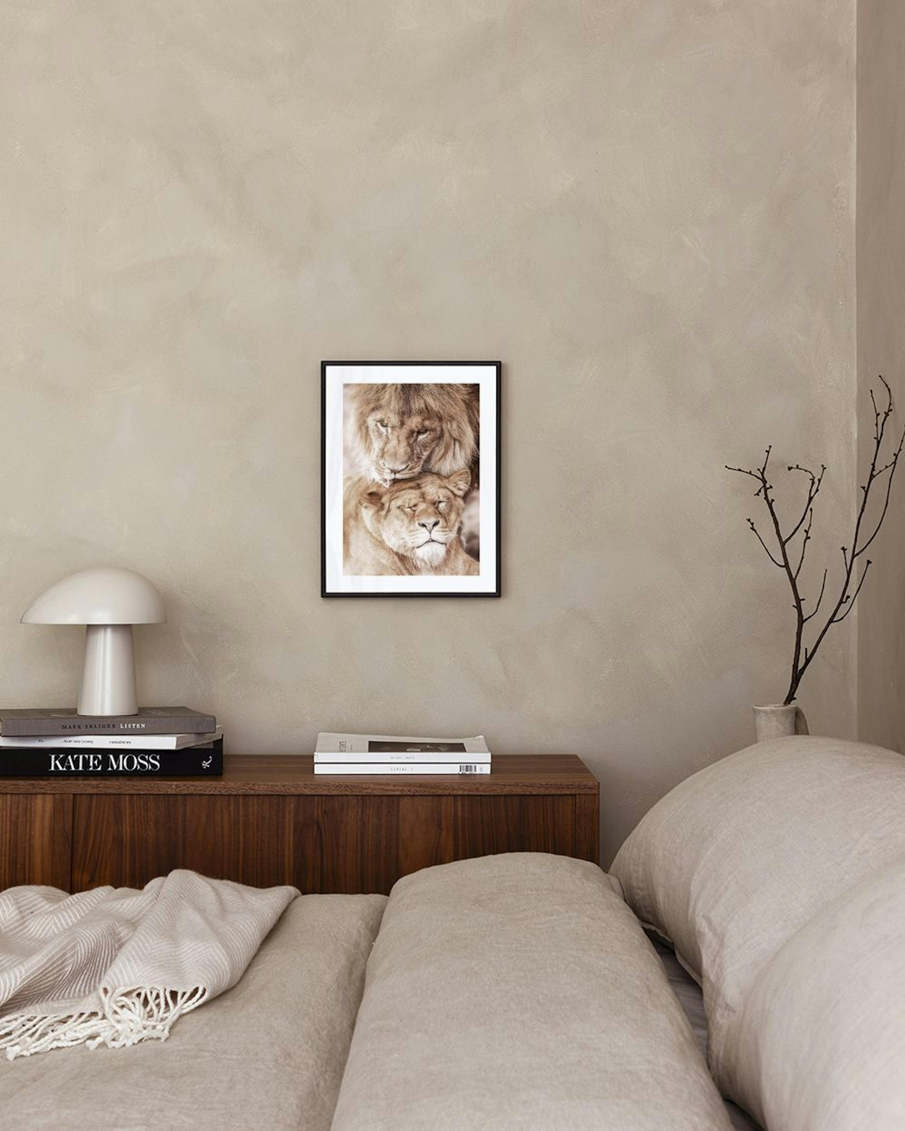 A print of a lion licking a lionesss head, displayed above a light beige armchair in a room.