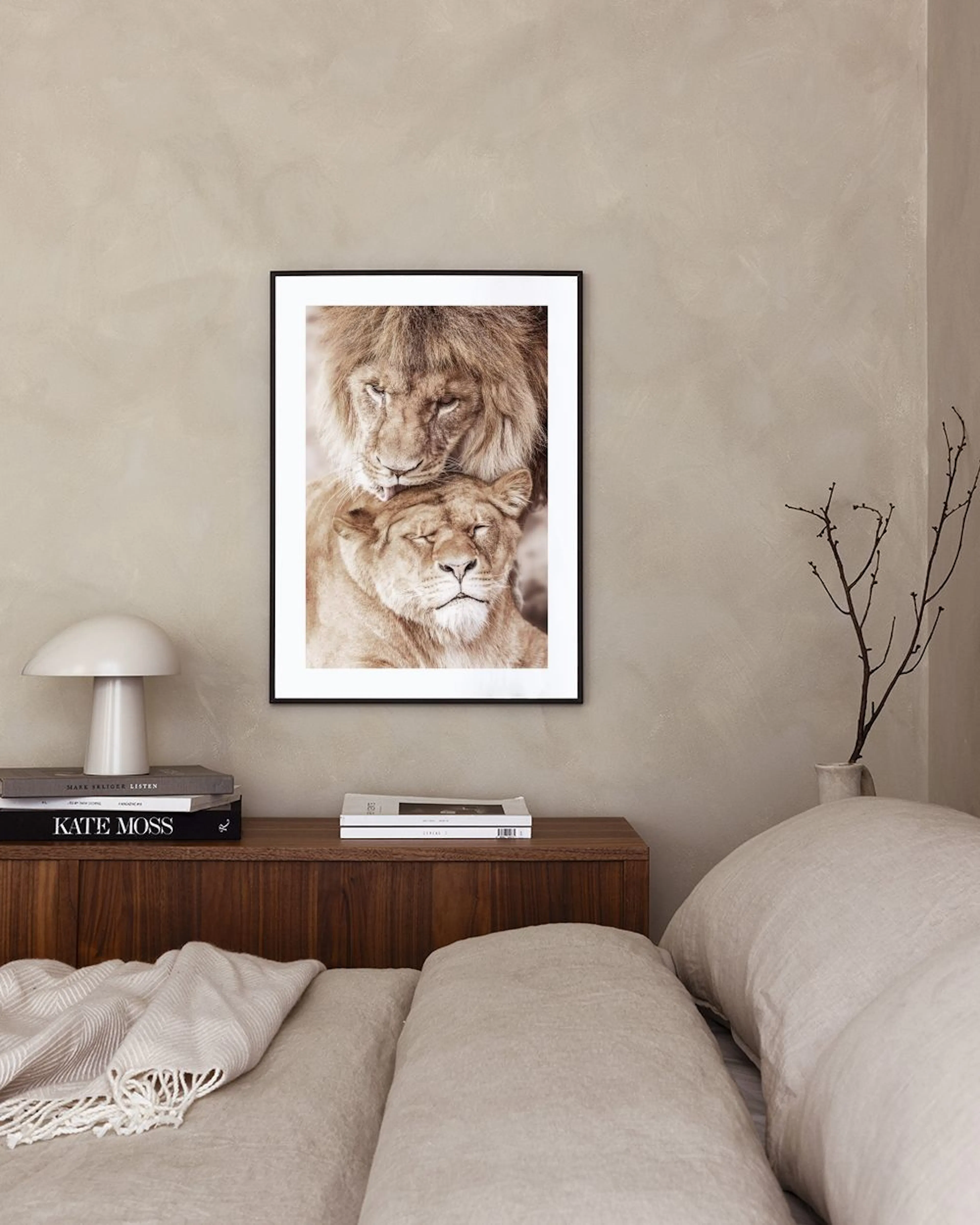 A print of a lion grooming a lioness, in sepia tones, displayed on a light grey wall next to a beige armchair.
