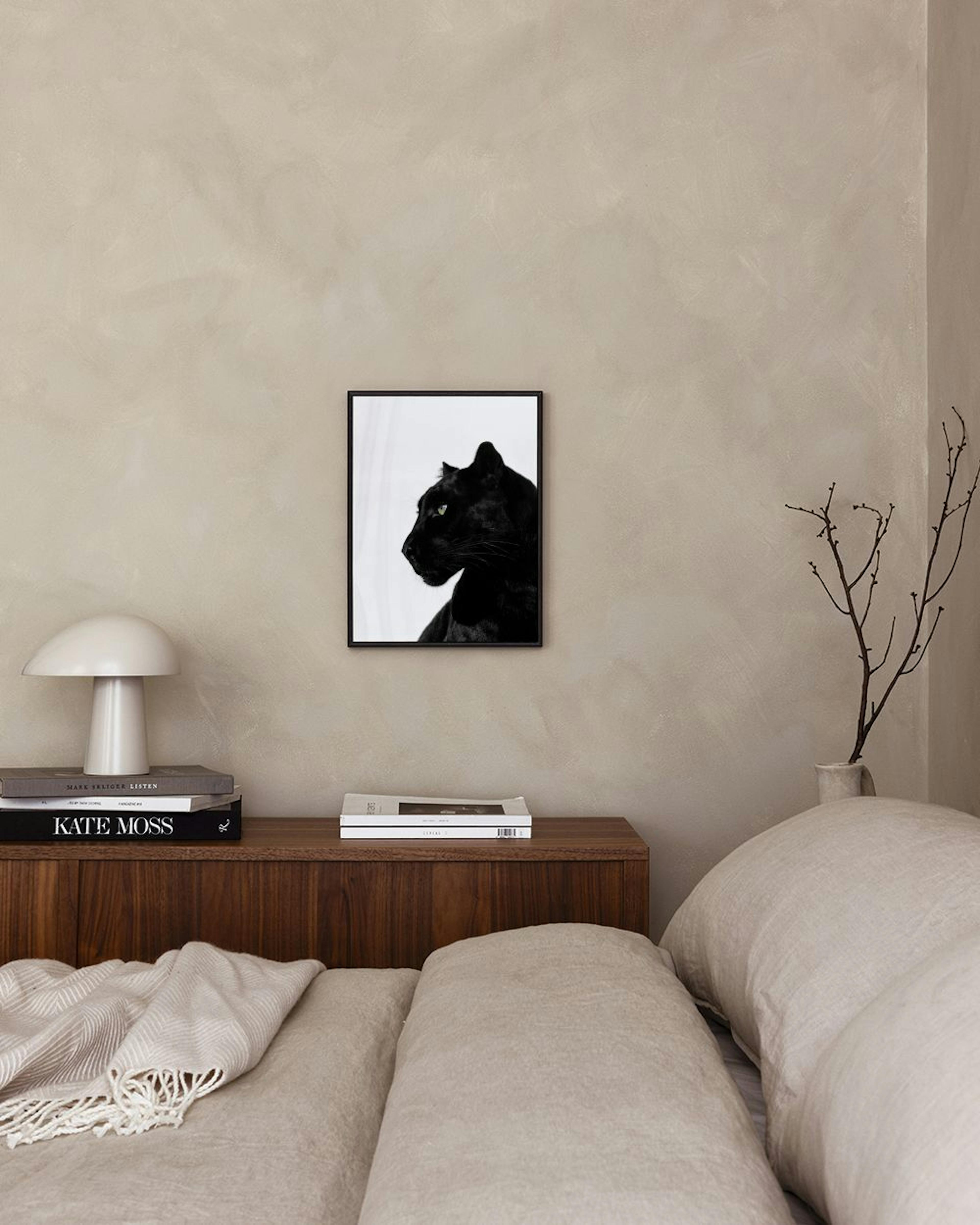 Affiche dune panthère noire aux yeux verts, accrochée au mur gris au-dessus dun tabouret en velours et dune table noire.
