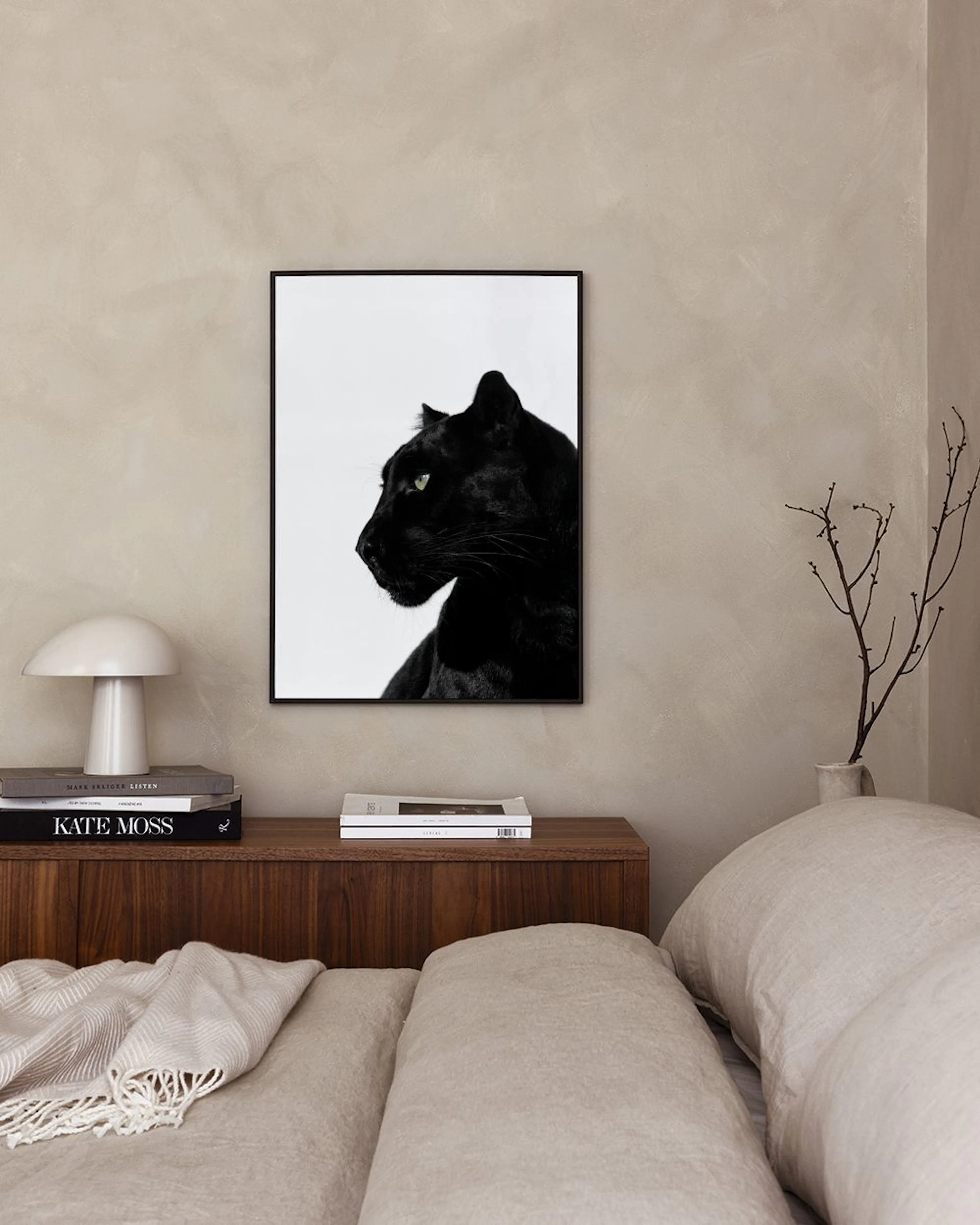 Poster av svart panter med gröna ögon i profil, hänger på en grå vägg ovanför en blå pall och ett svart sidobord.