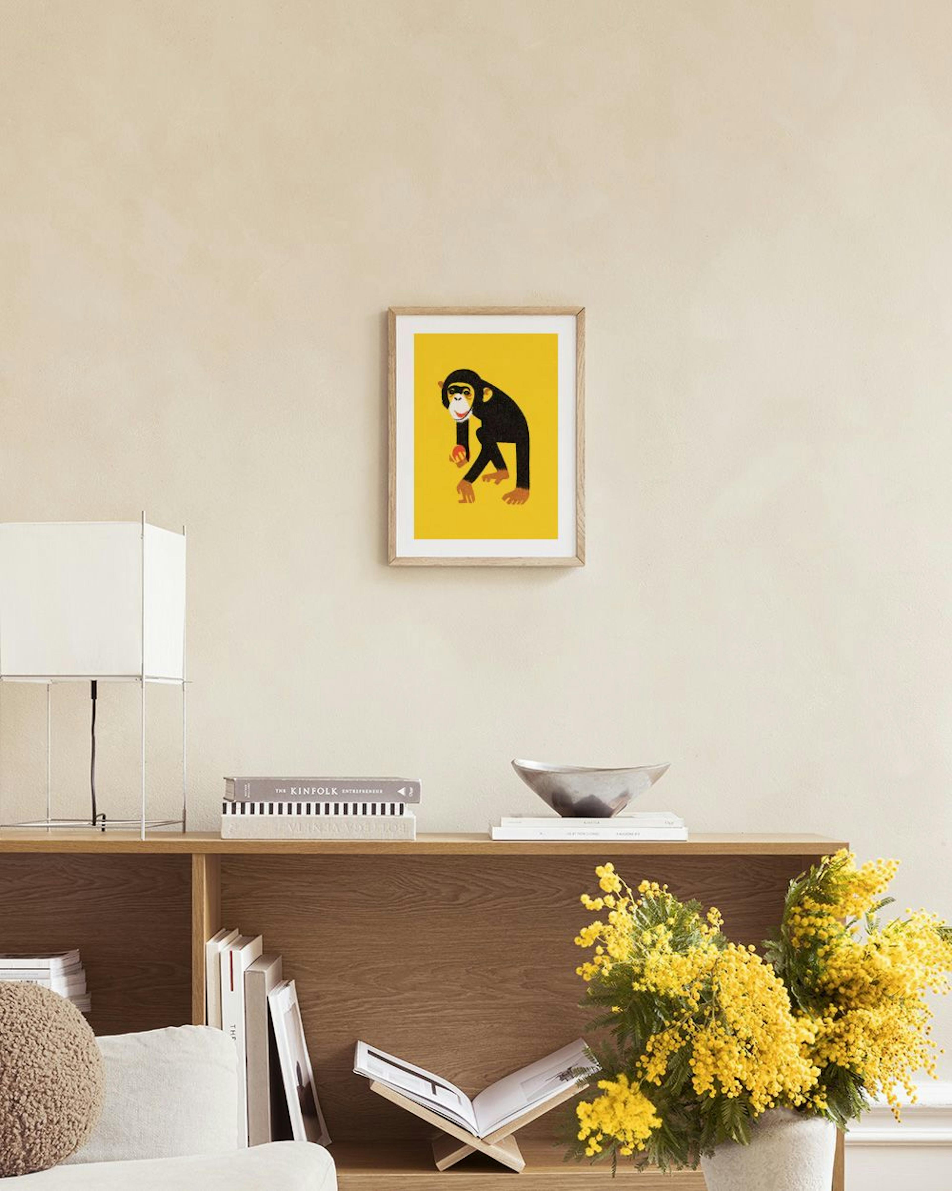 Póster de un mono negro con una manzana roja, sobre un fondo amarillo, en una pared blanca encima de un mueble.